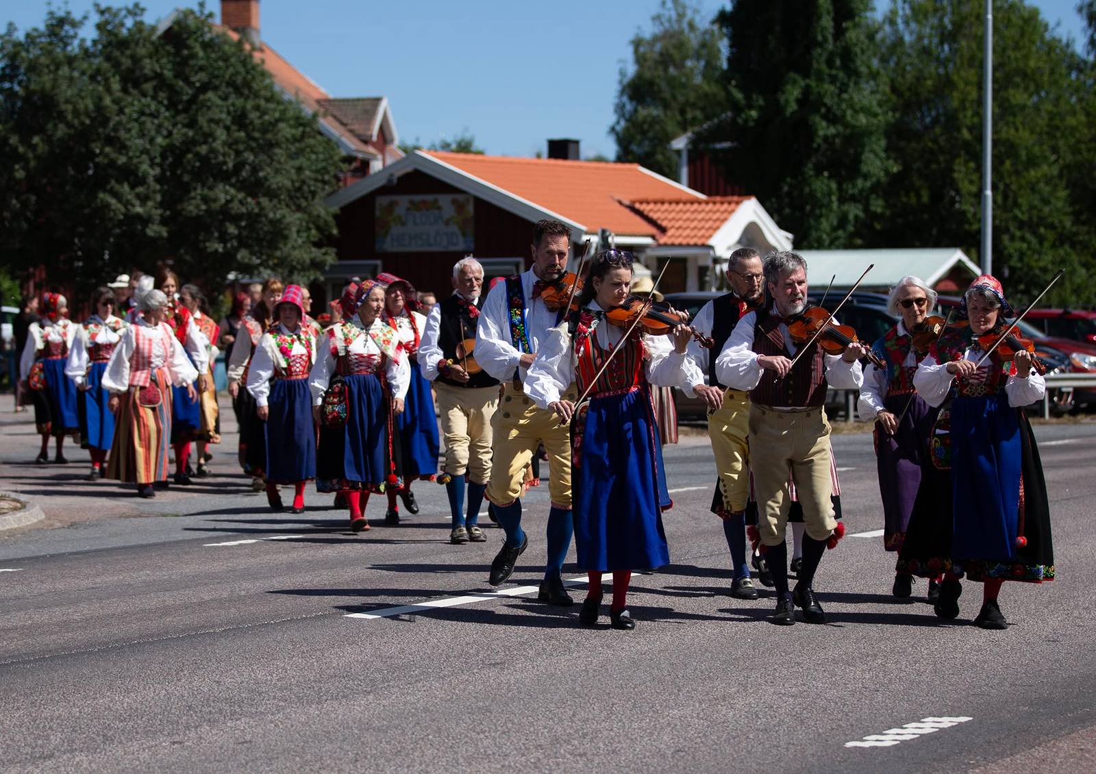 Spelmän och folkdräktsklädda i tåg längs byvägen under Komidsommarfesten.