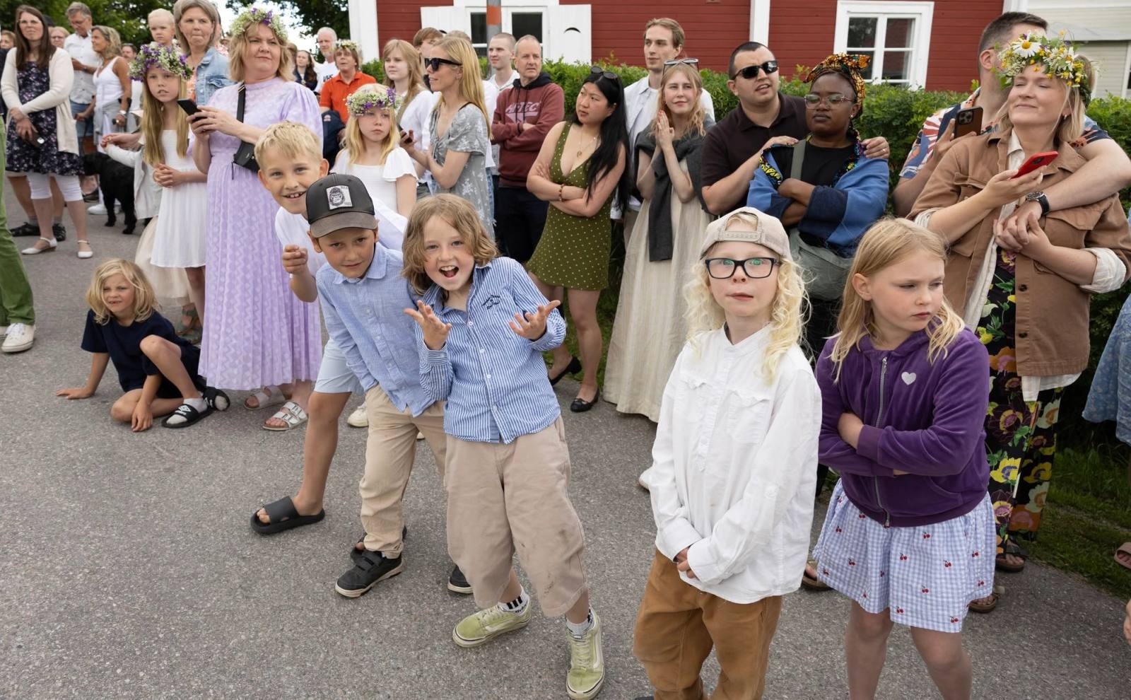 Barn i främre ledet av folksamlingen vid midsommarfirandet, några med blomsterkrans i håret.