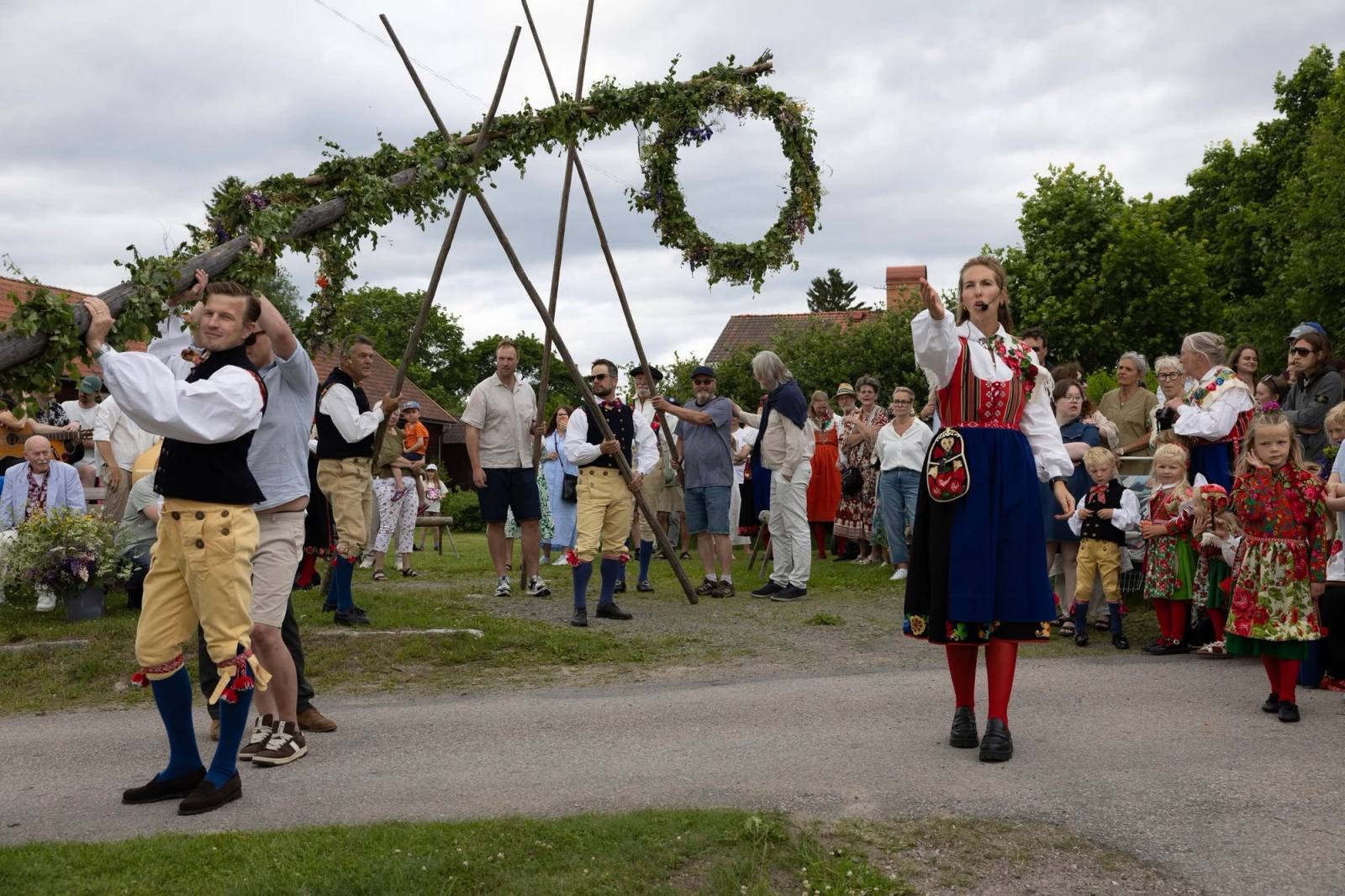 Midsommarstången reses medan folk i folkdräkt står runt omkring.
