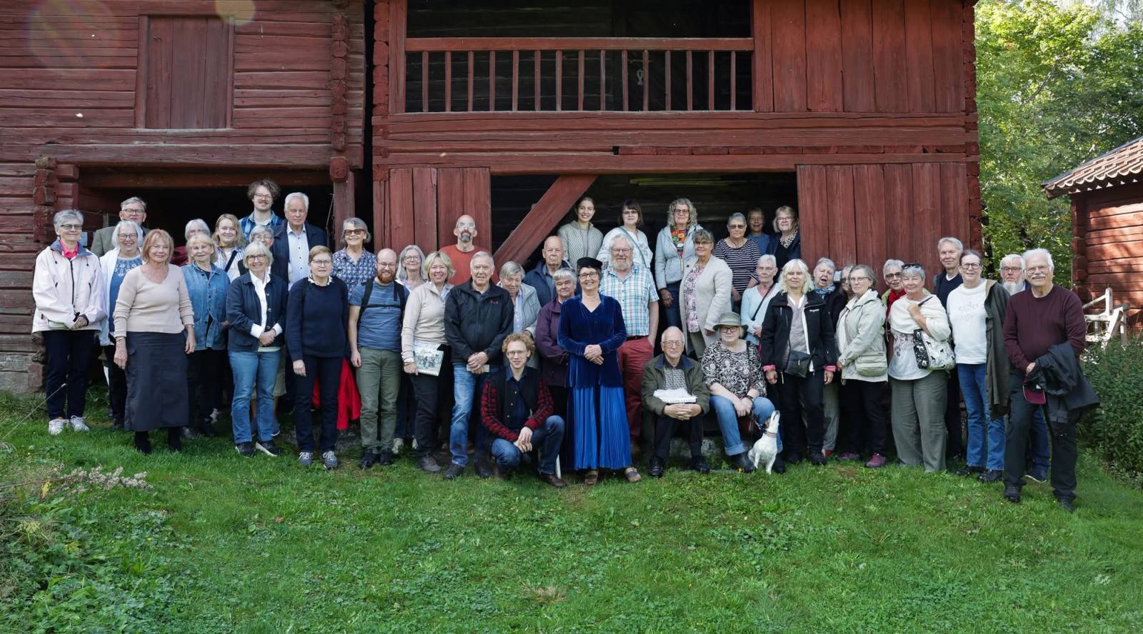 Ett stort gäng bybor uppställda för gruppfoto framför en röd timmerbyggnad.