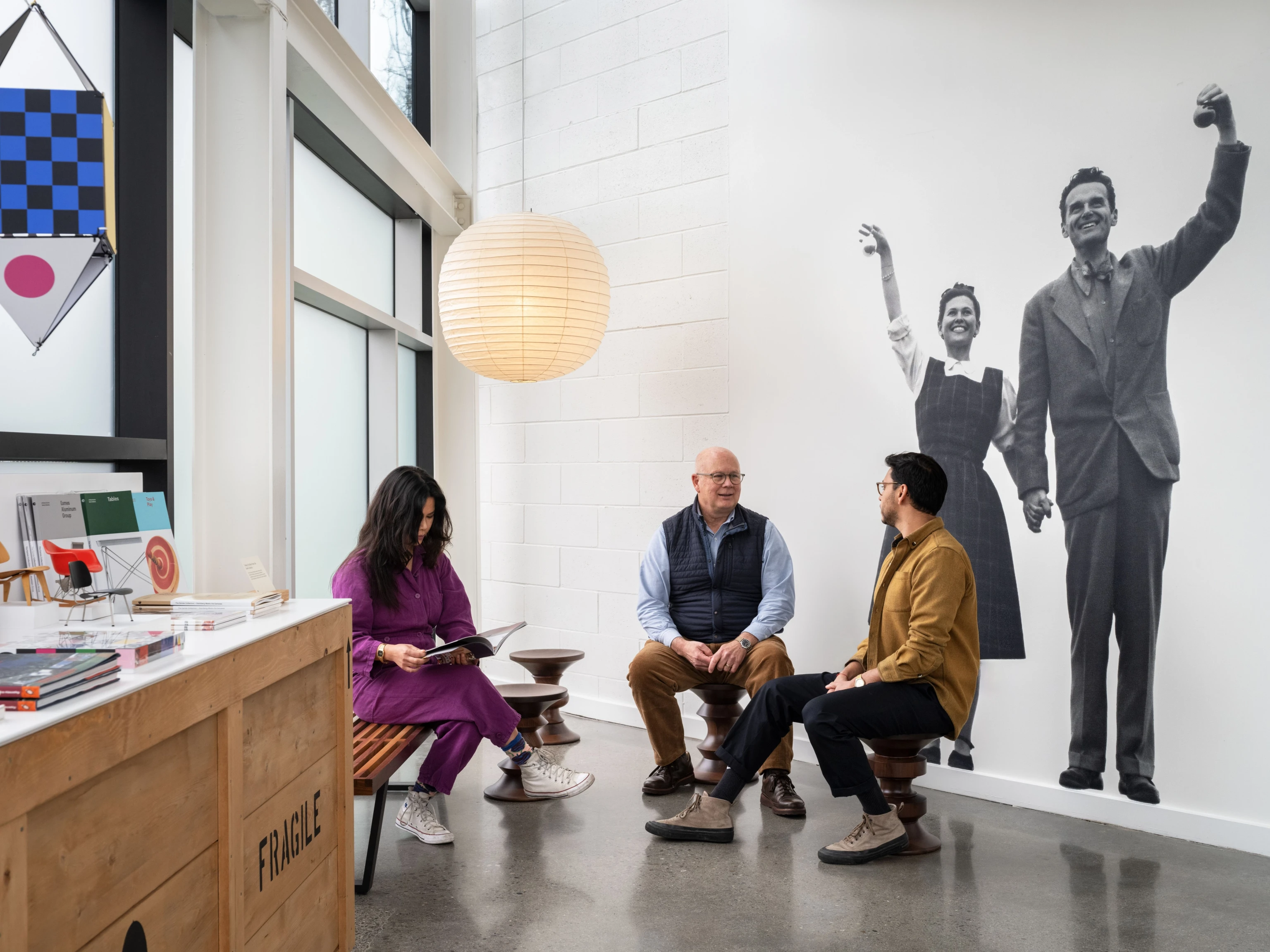 Visitors at the Eames Institute seated together with a large image of Ray and Charles Eames in the background.