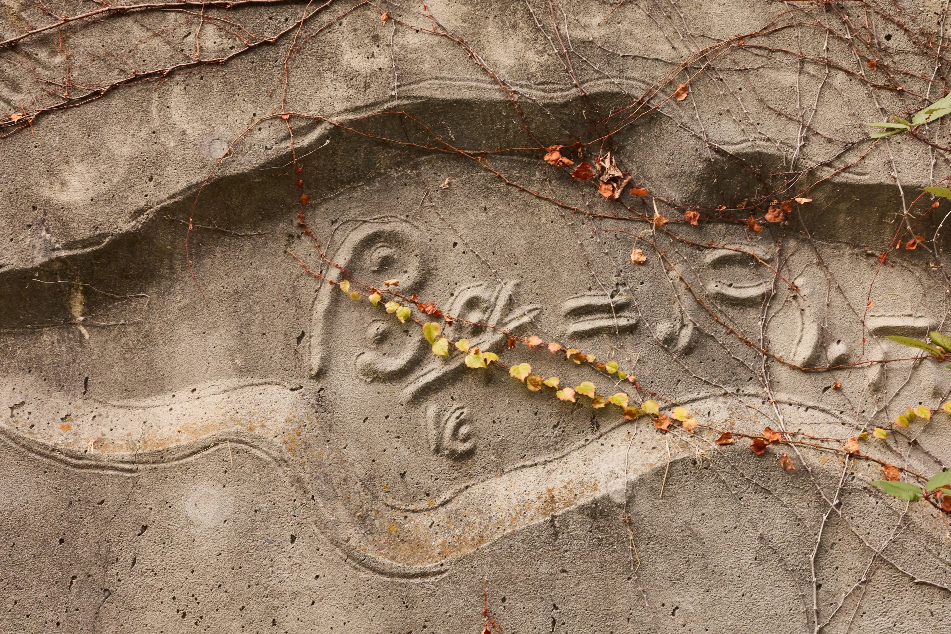 Detail view from a carved concrete relief mural by artist Gurdon Woods featuring symbolic marks.