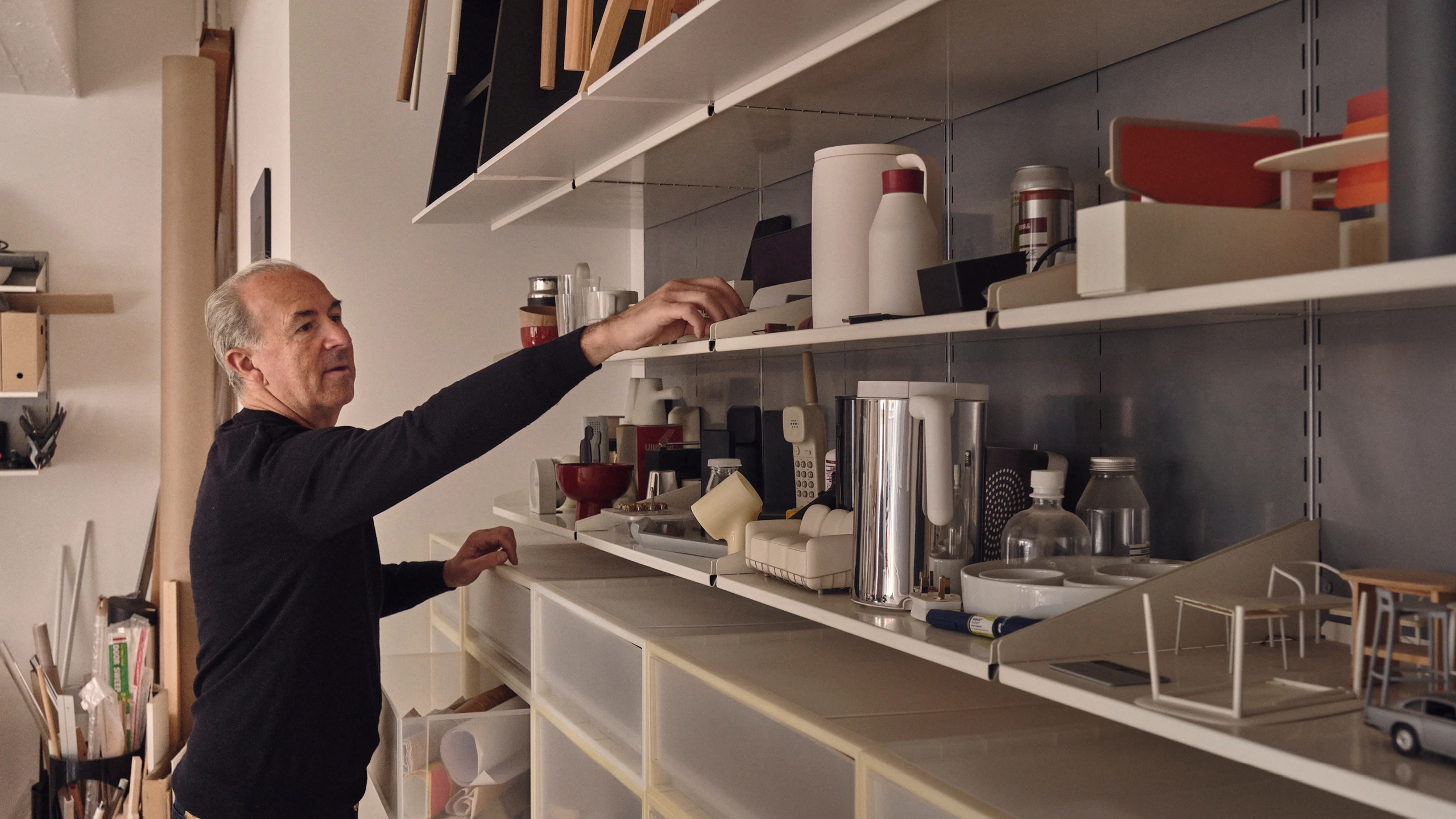 Sam Hecht of design studio Industrial Facility reaching for designs and prototypes on shelves—Kazam! Magazine.