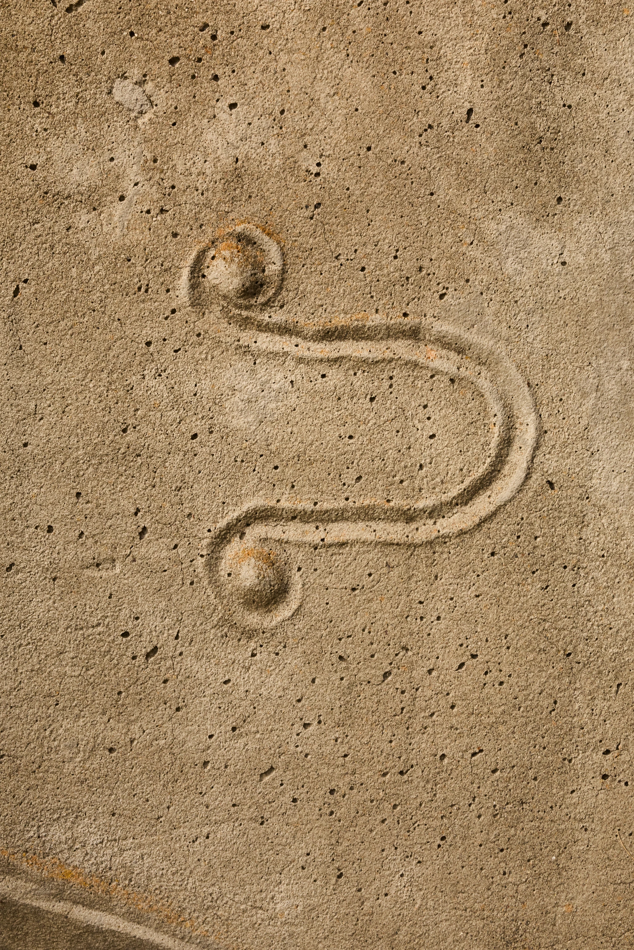 Close up from a carved concrete relief mural by artist Gurdon Woods featuring a u-shaped mark.