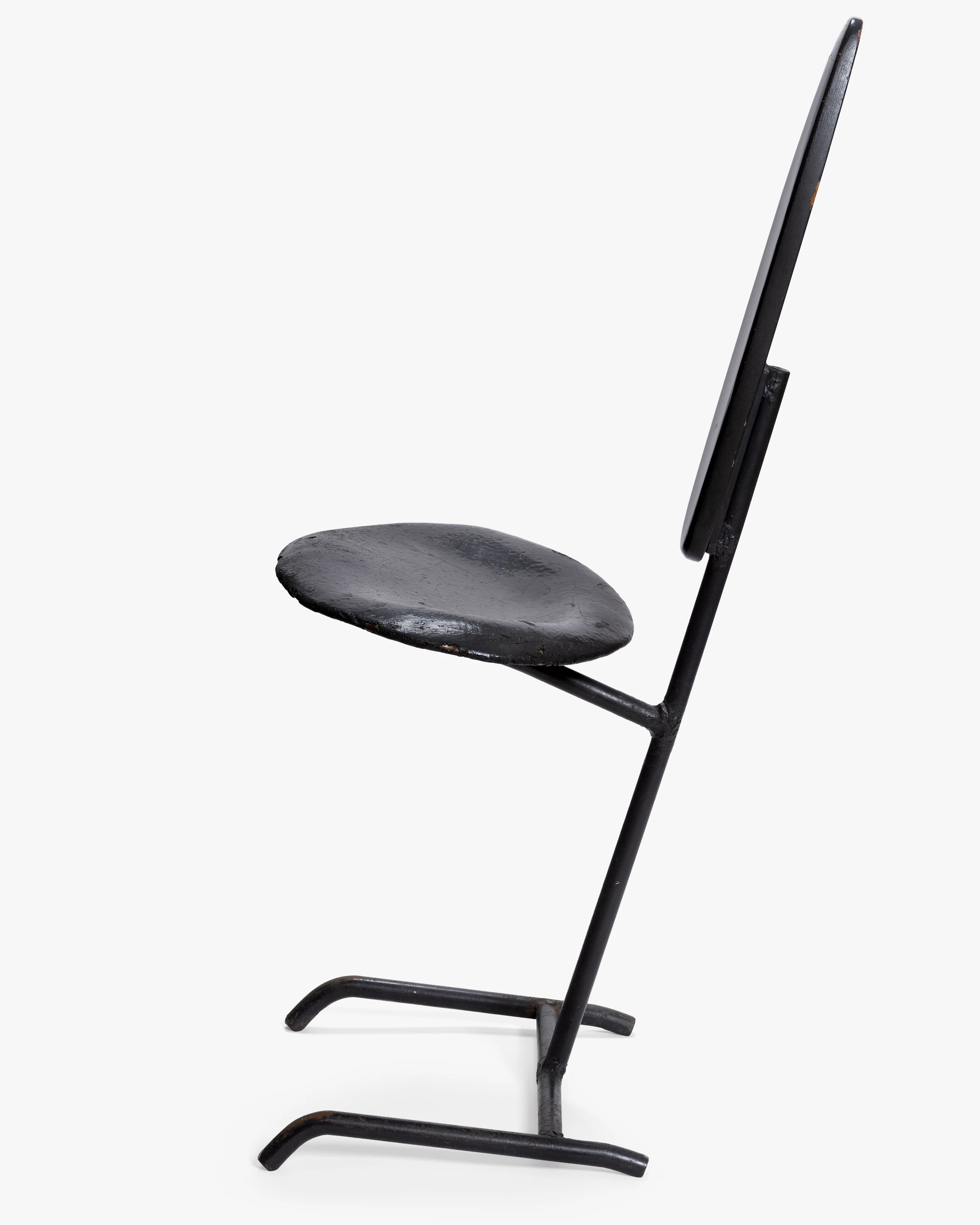 Side view of the Eames Minimum Chair. The design is slender and made of two oval pieces of sheet metal and a metal rod base.