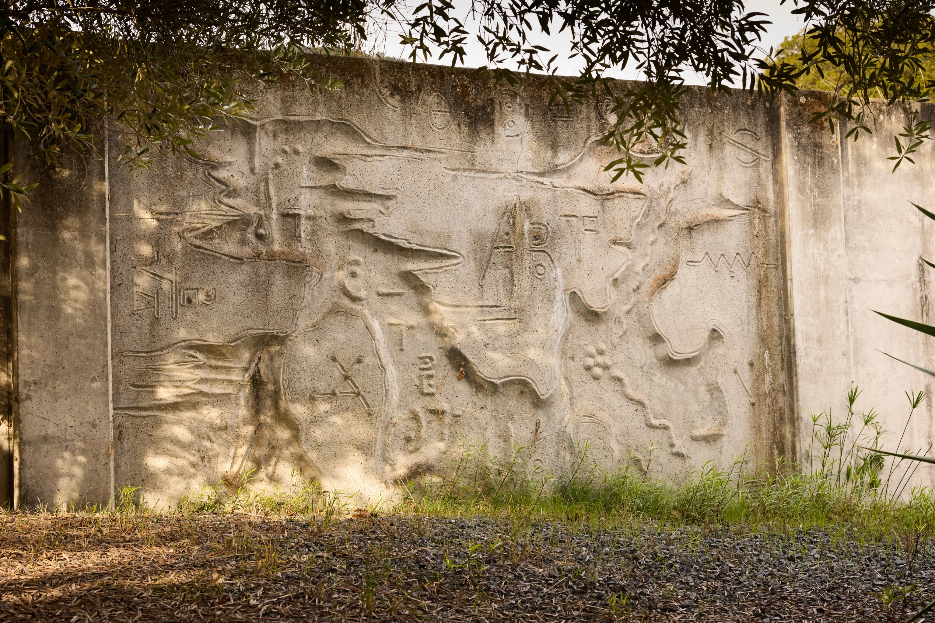 A carved concrete relief mural by artist Gurdon Woods featuring several organic and geometric marks.