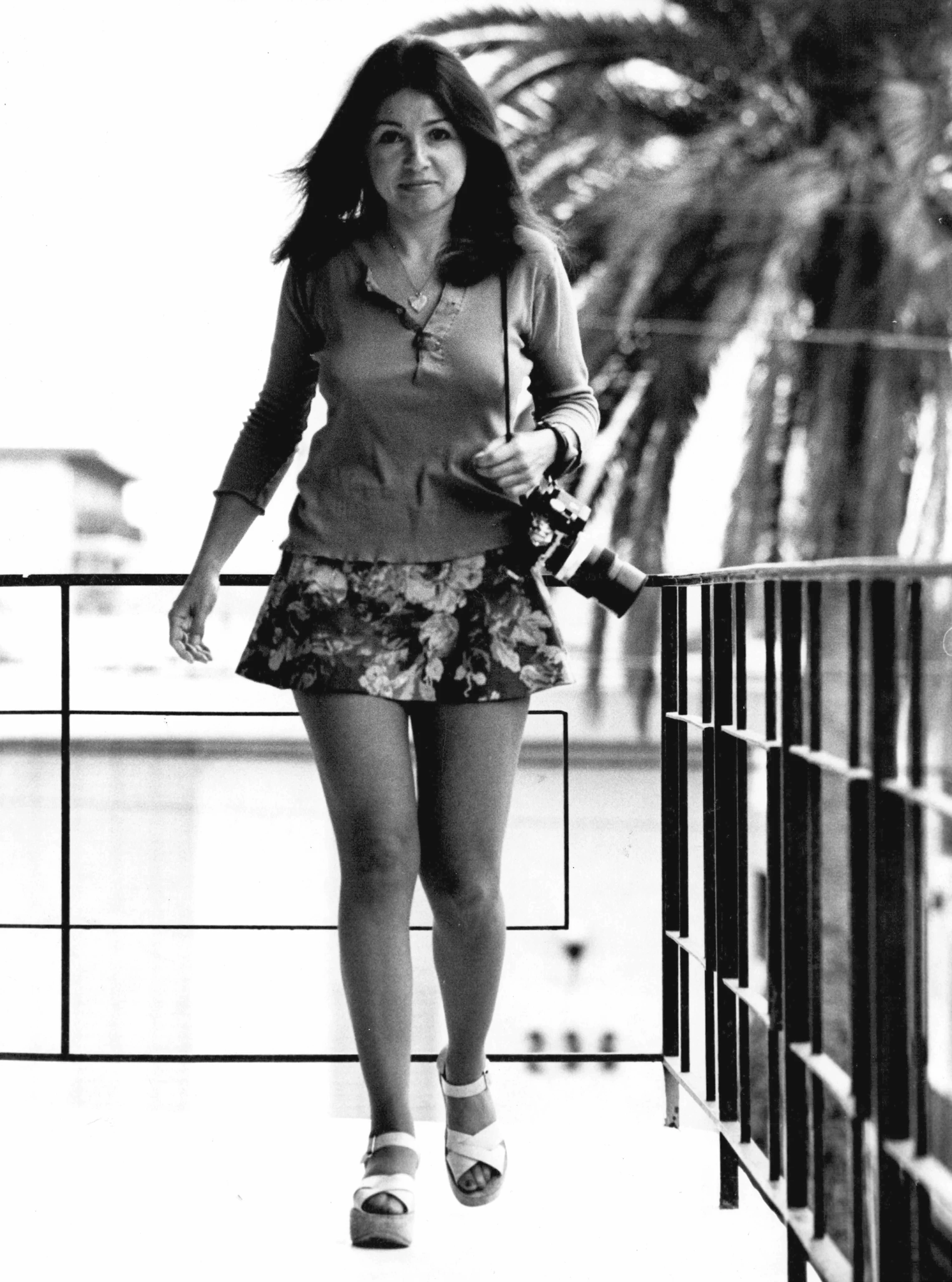 Annette Del Zoppo carrying her camera, and walking with palm trees in the background.