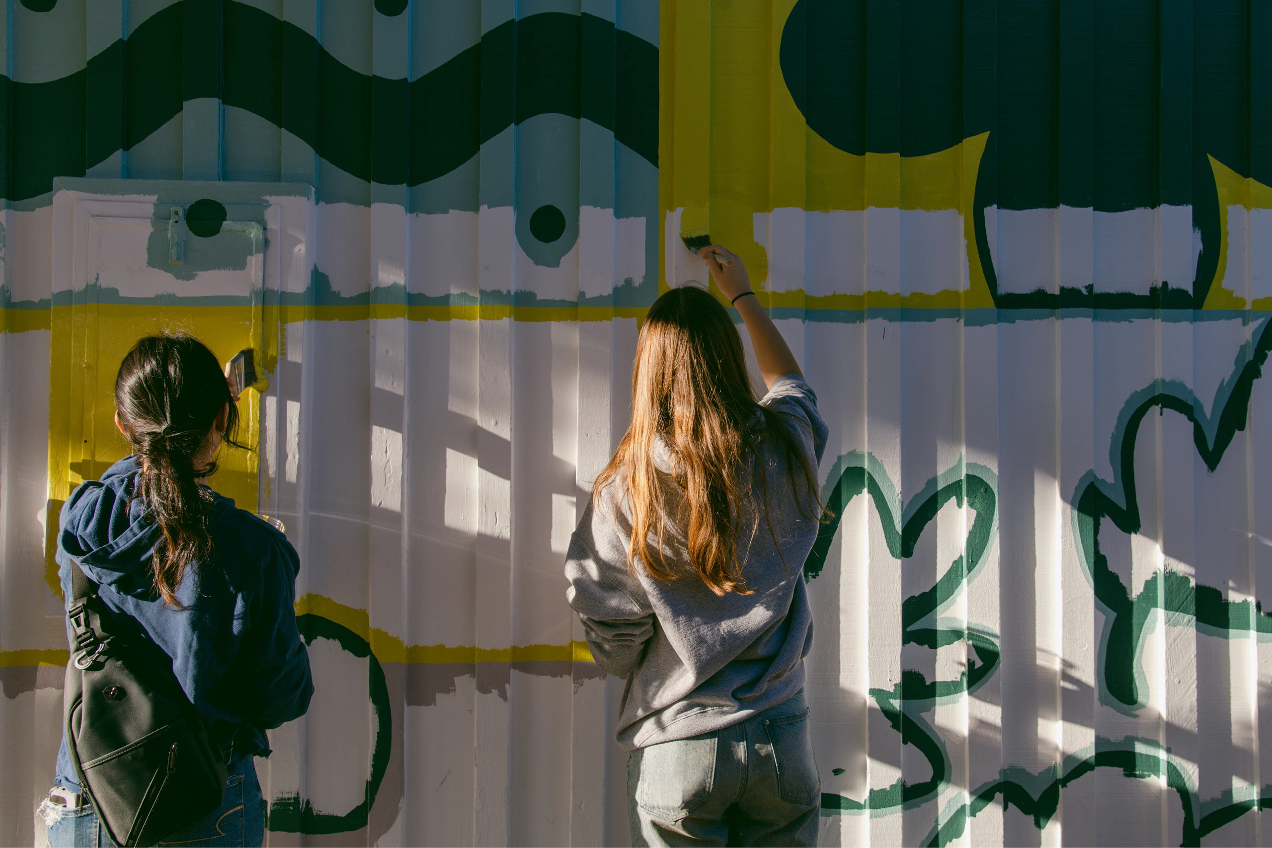 Two Project Color Corps volunteers painting a mural.
