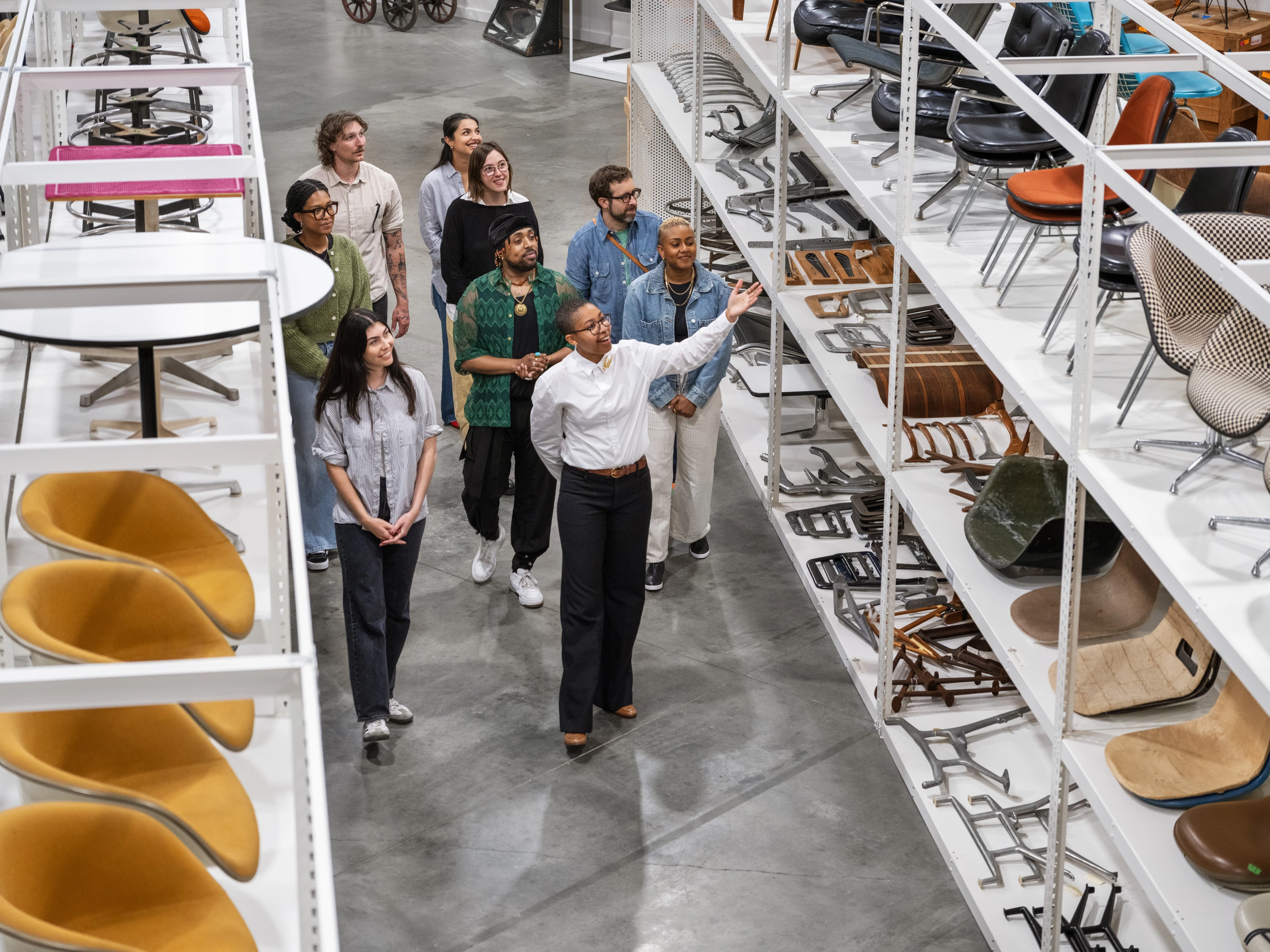 A docent gives a tour of the Eames Institute archives to guests among shelves filled with Eames furniture designs.
