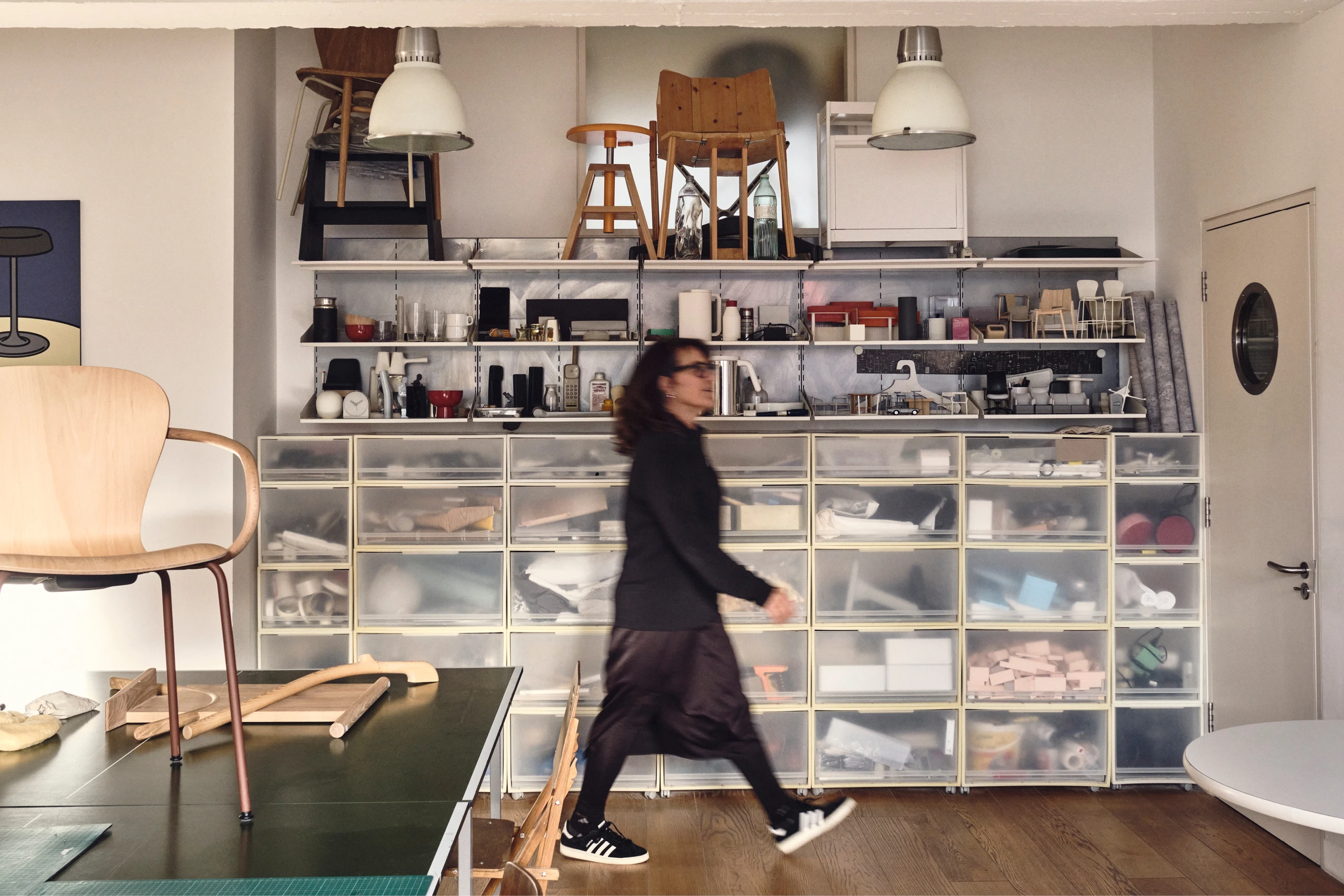 Kim Colin of design studio Industrial Facility walking past shelves with many objects and prototypes designed by the firm.