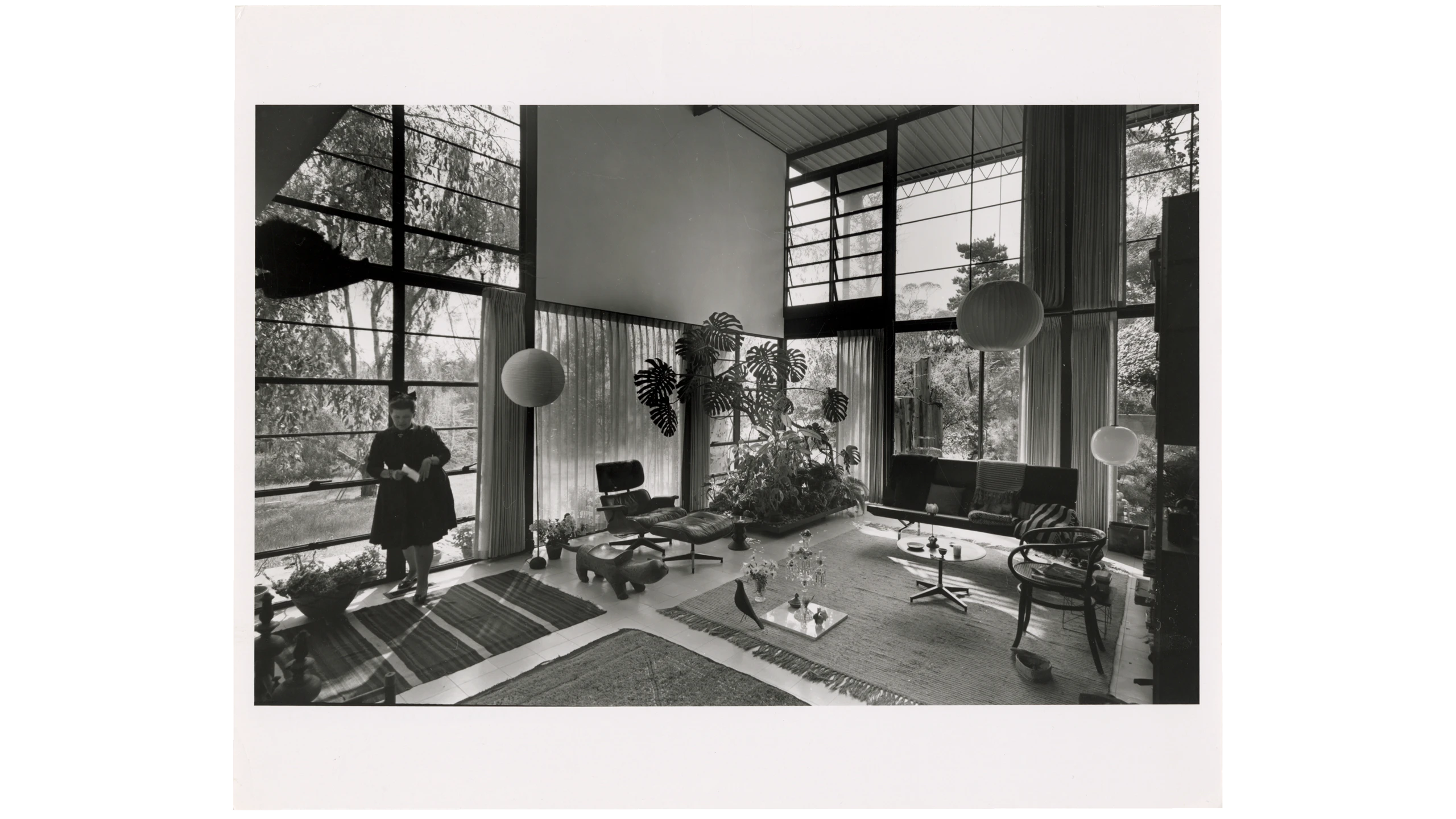 Ray Eames in the interior of Case Study House 8 featuring many Eames furniture designs.
