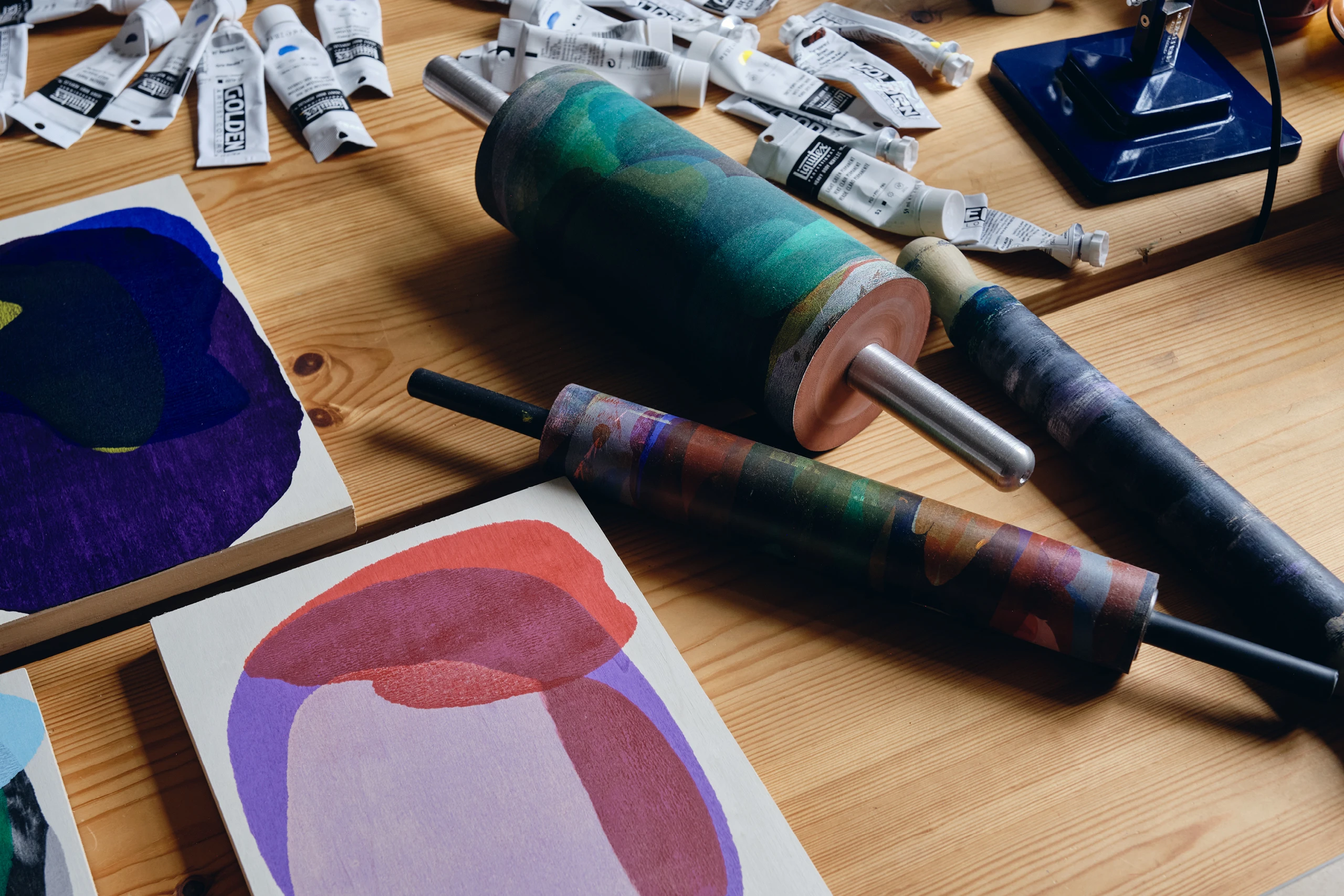 Artist Daniel Eatock’s work table in his London art studio featuring various rolling pin paintings, rolling pins, and paints.
