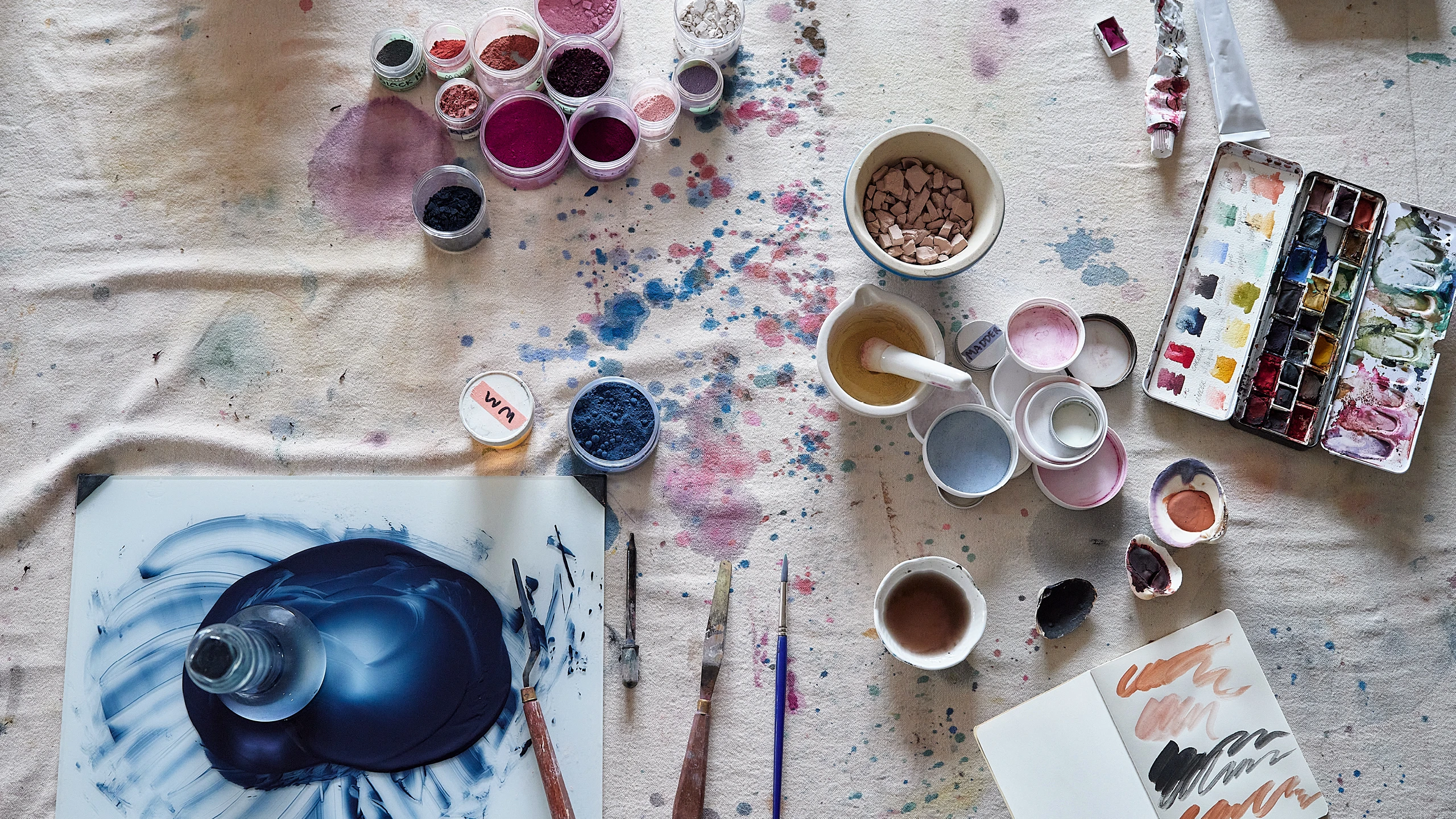 A glimpse of watercolor production at abstract artist Natalie Stopka’s studio shows pigments, grinding slab and muller, paint pans, and paint swatches.