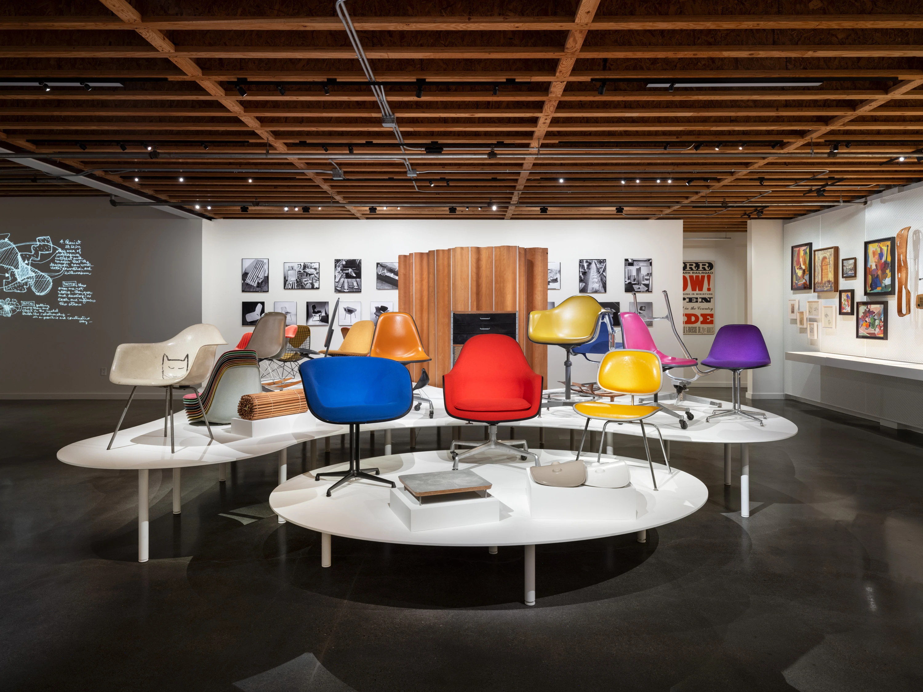 Interior view of the Eames Institute archives with several pieces of Eames furniture on pedestals and art on the walls.