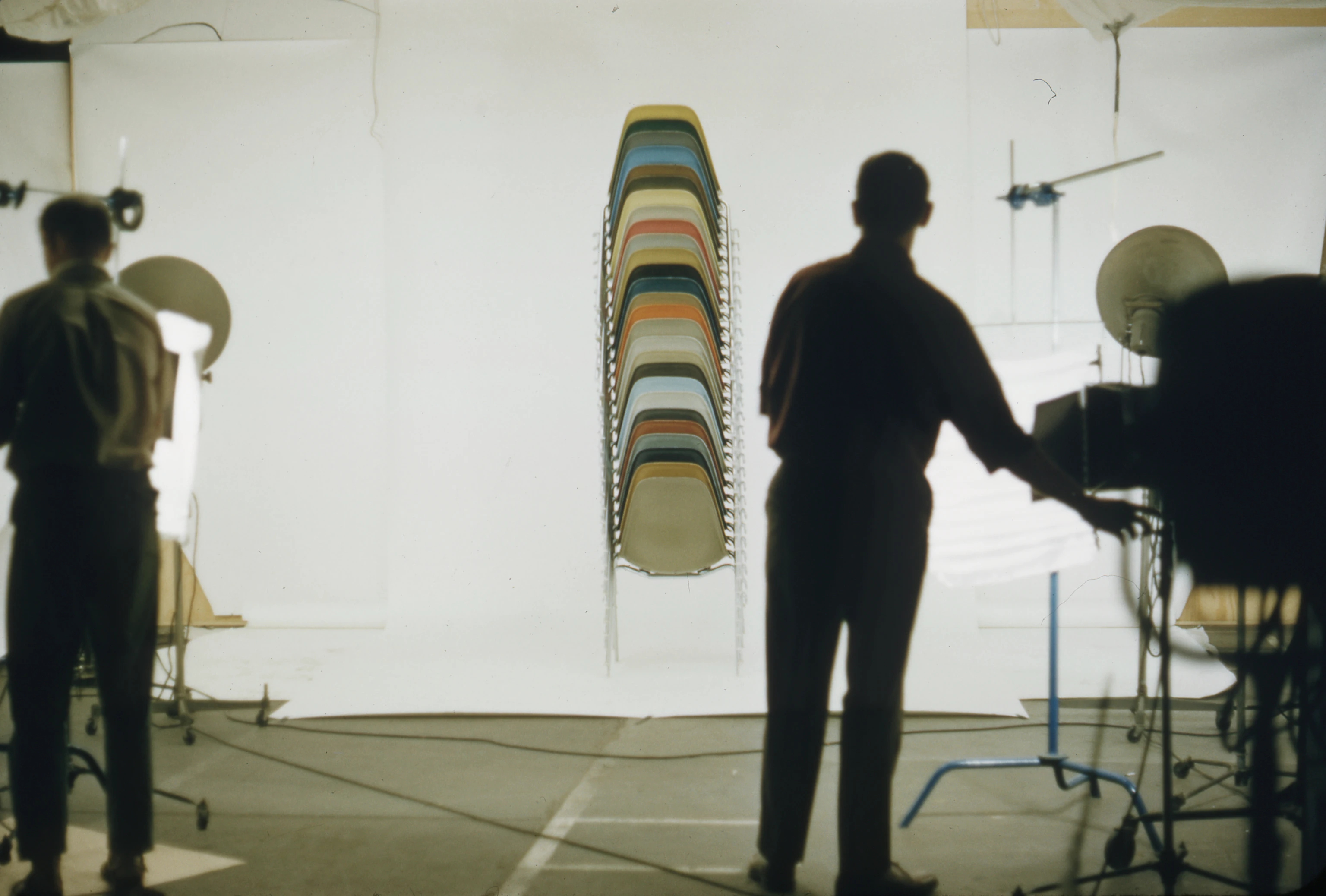 Charles Eames and a staff member in 1960 photographing a tall stack of DSS Eames chairs in various colors (dining side stacking chairs) at the Eames office in Venice, CA.