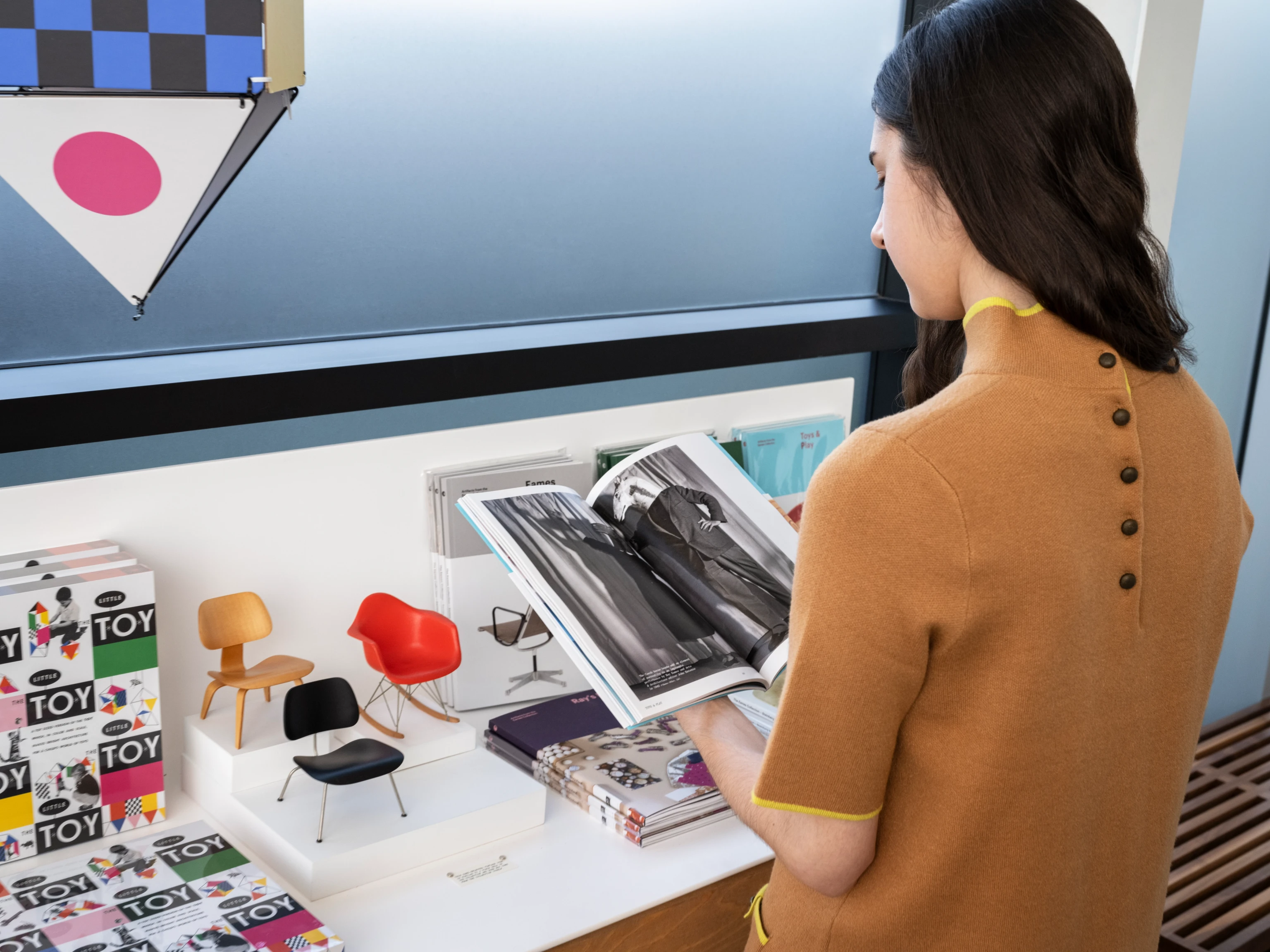 A woman in a mustard top browsing books and other objects in the Atrium Shop at the Eames Archives