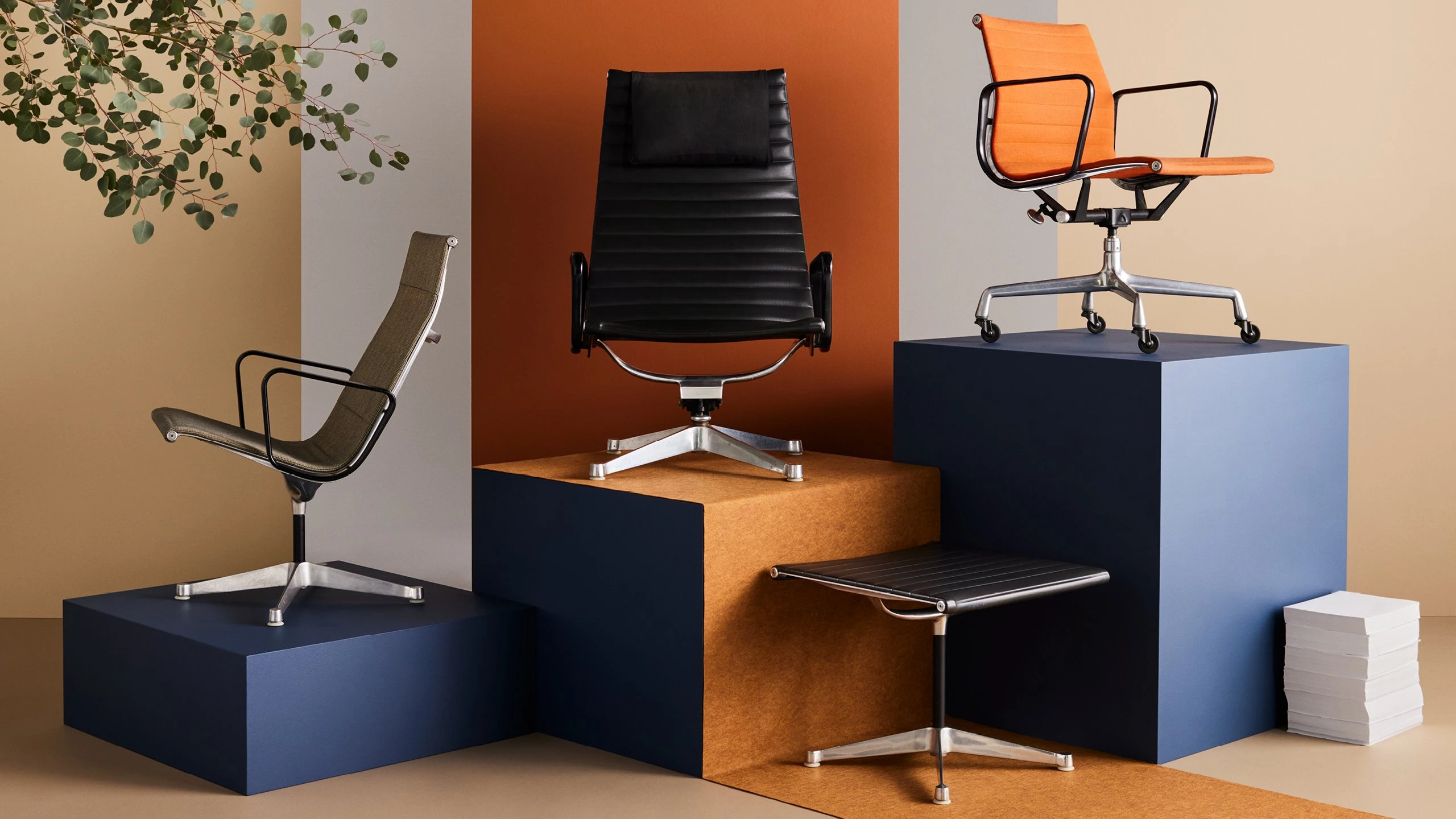 Eames Aluminum Group desk chair, lounge chairs, and ottoman placed on colorful pedestals.