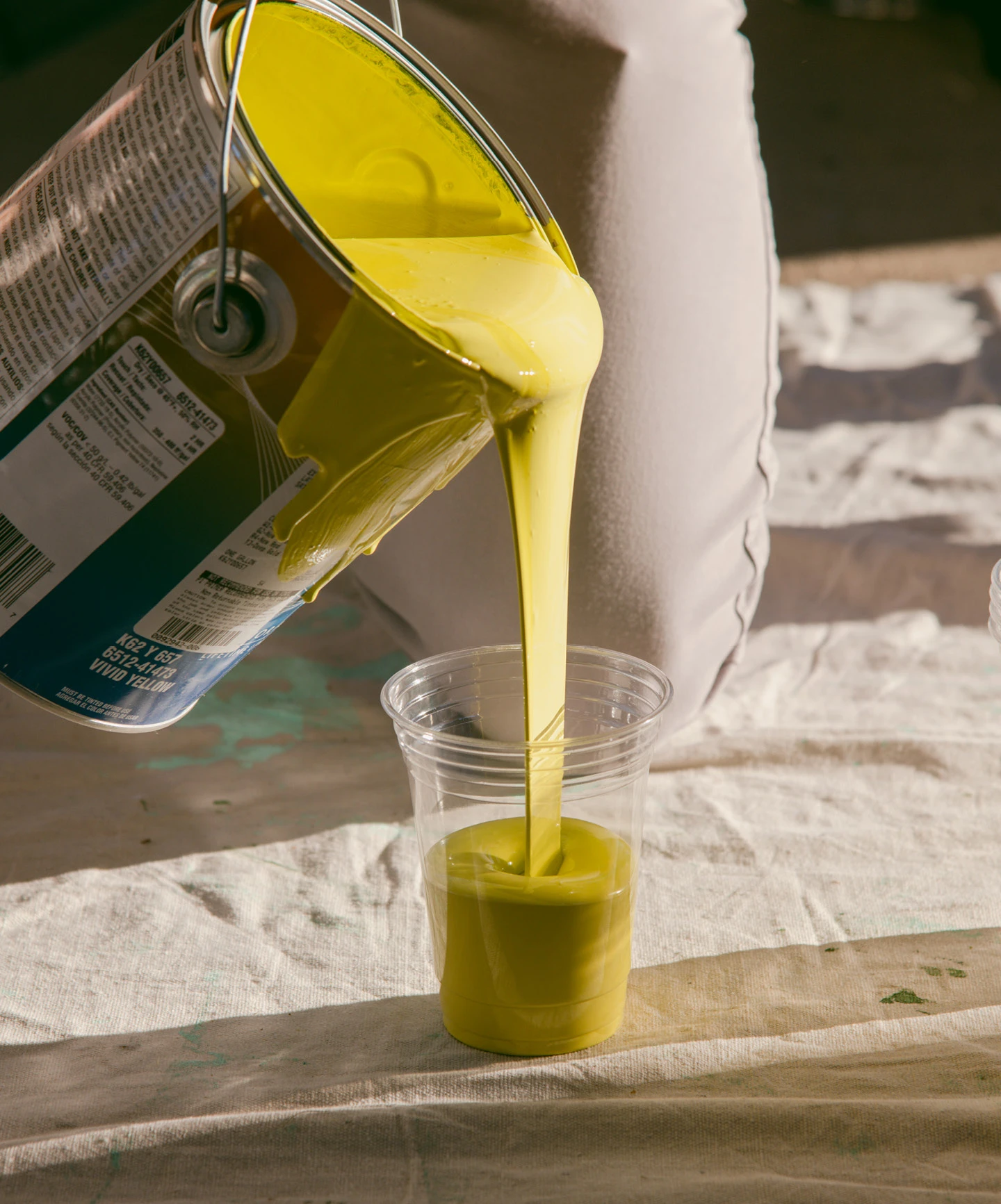 Gallon of yellow paint being poured into a cup at the sight of a Project Color Corps mural.
