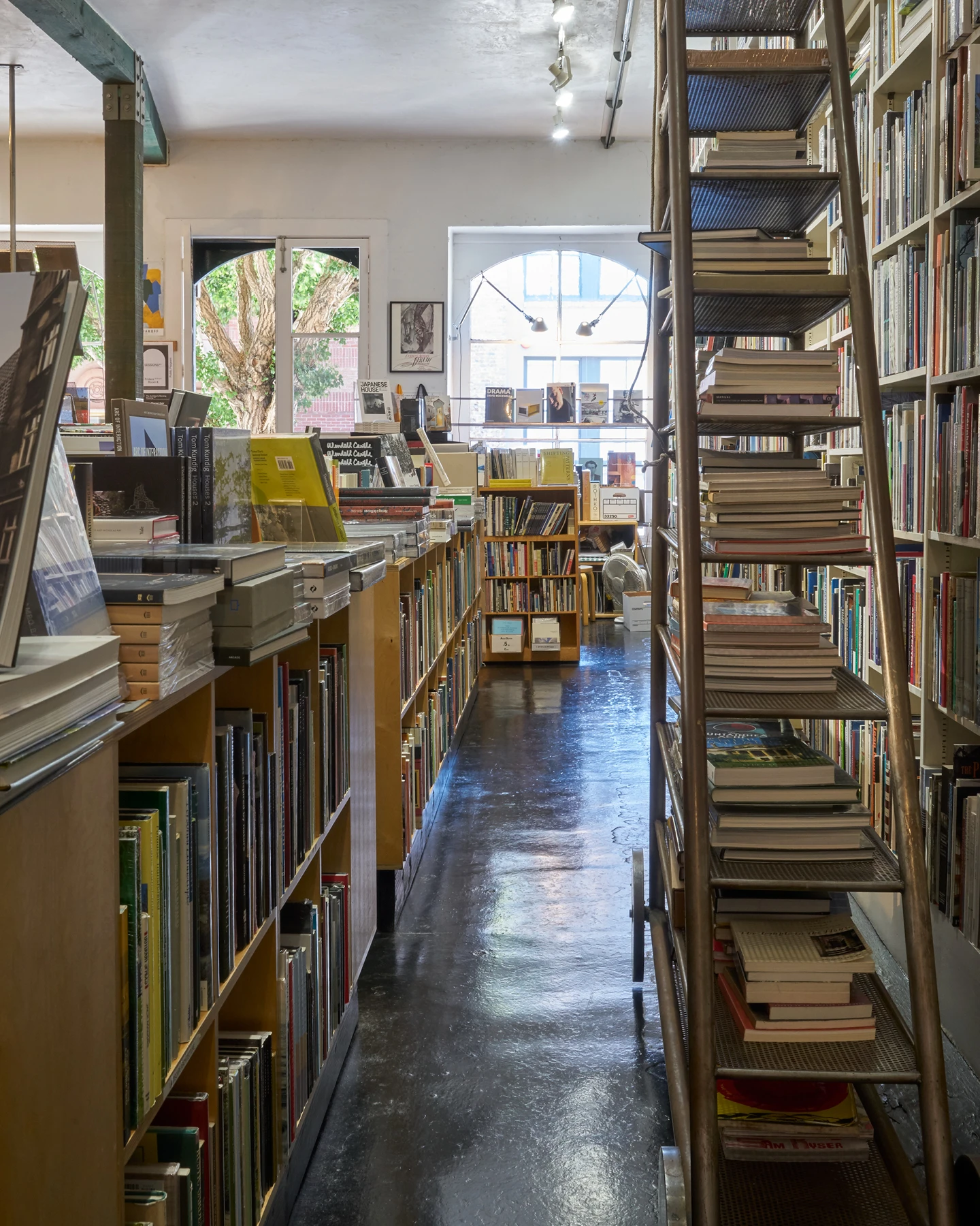 Stacks of architectural books on display on top of full bookshelves and a ladder.
