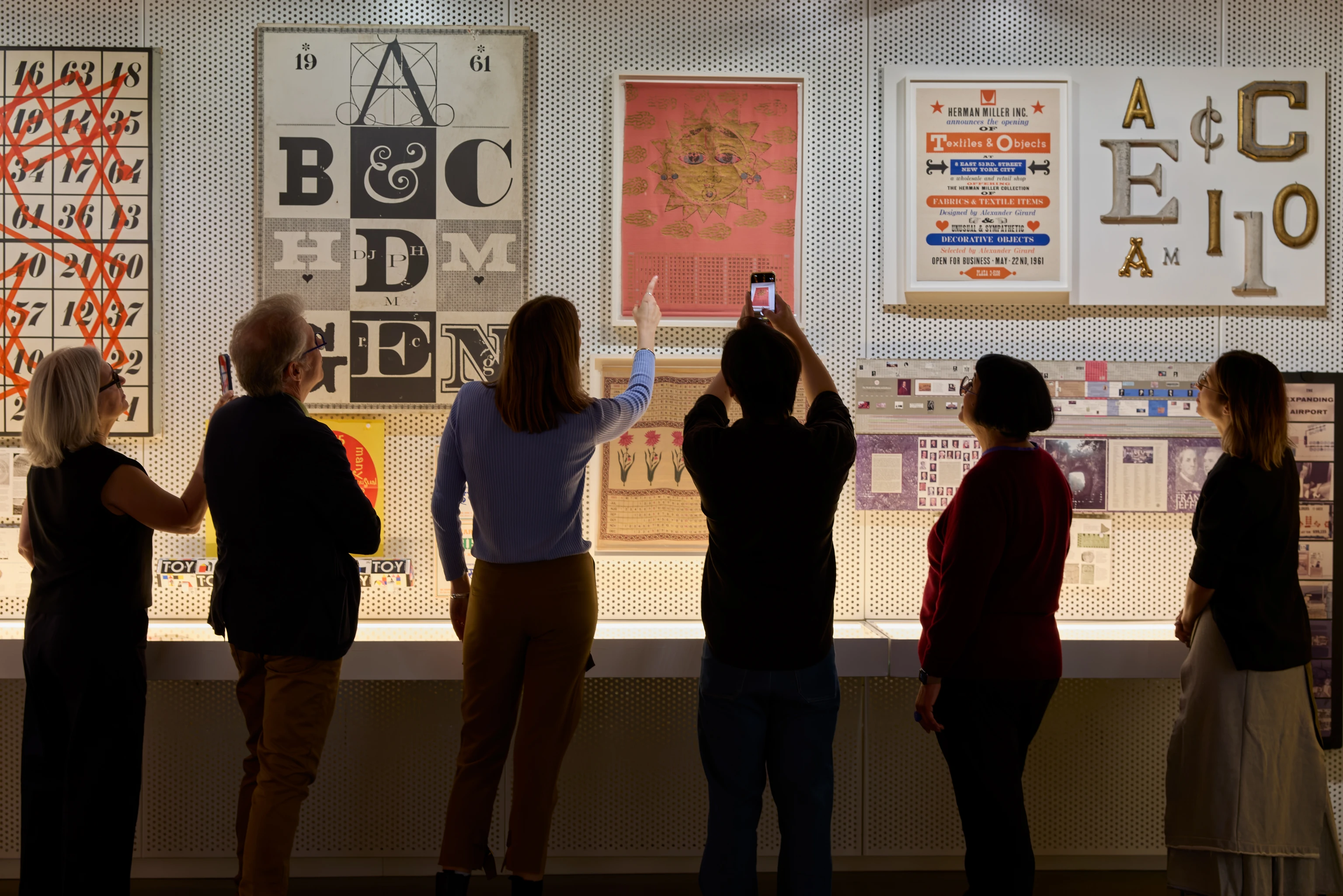 Visitors explore the Work Gallery at the Eames Institute, viewing graphic designs, exhibition materials and archival objects.