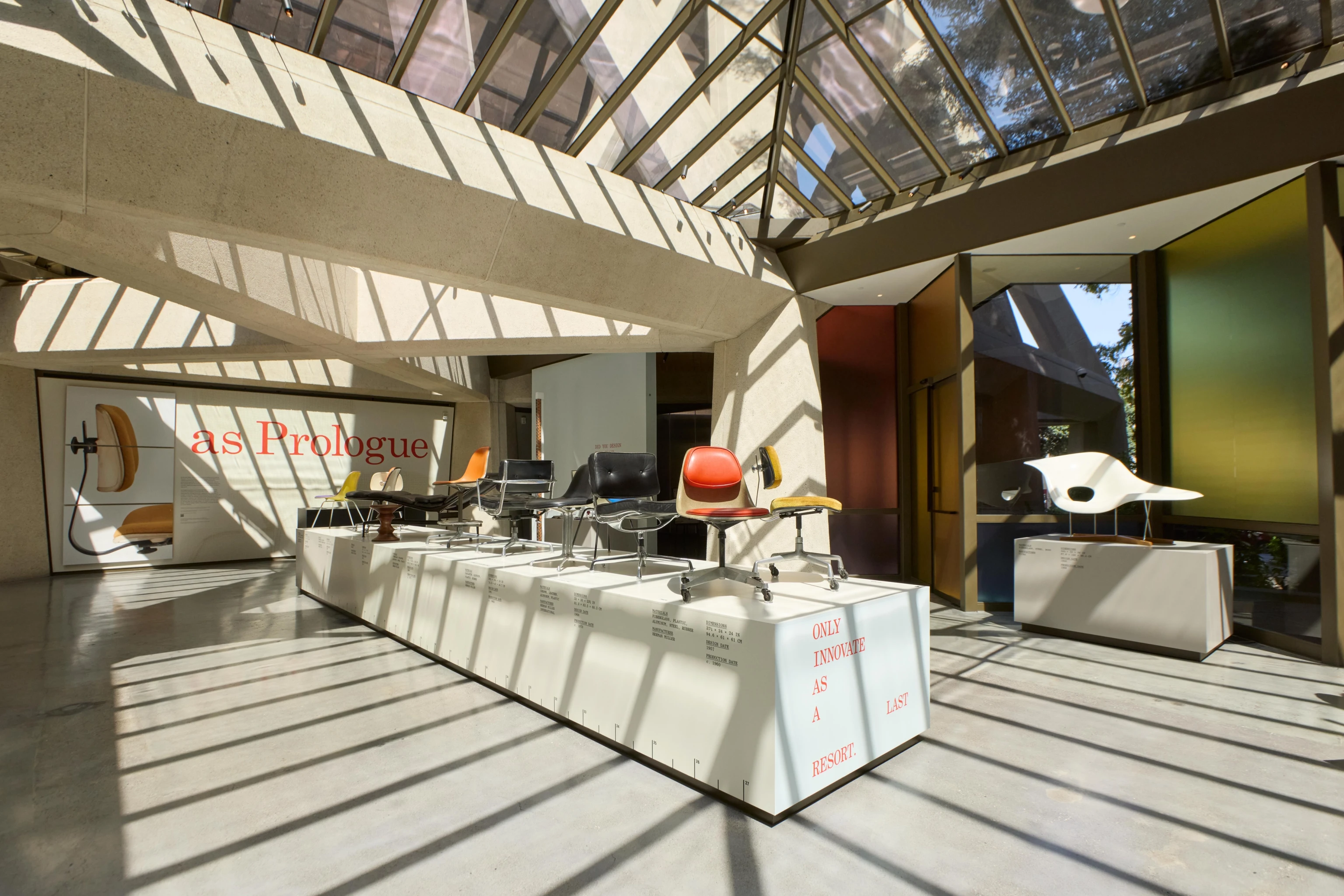 Interior view of the Past as Prologue exhibition at the Transamerica Pyramid Annex Gallery featuring many Eames chairs on a large platform.
