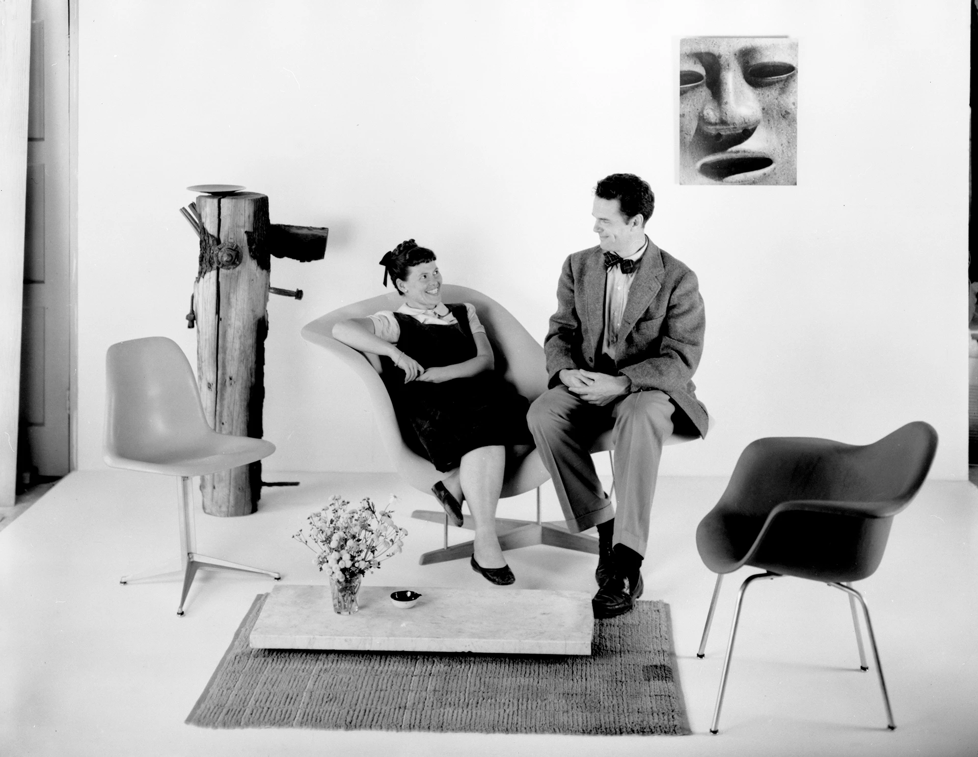 Ray and Charles Eames sitting on the La Chaise chair prototype along with two fiberglass Eames shell chairs.