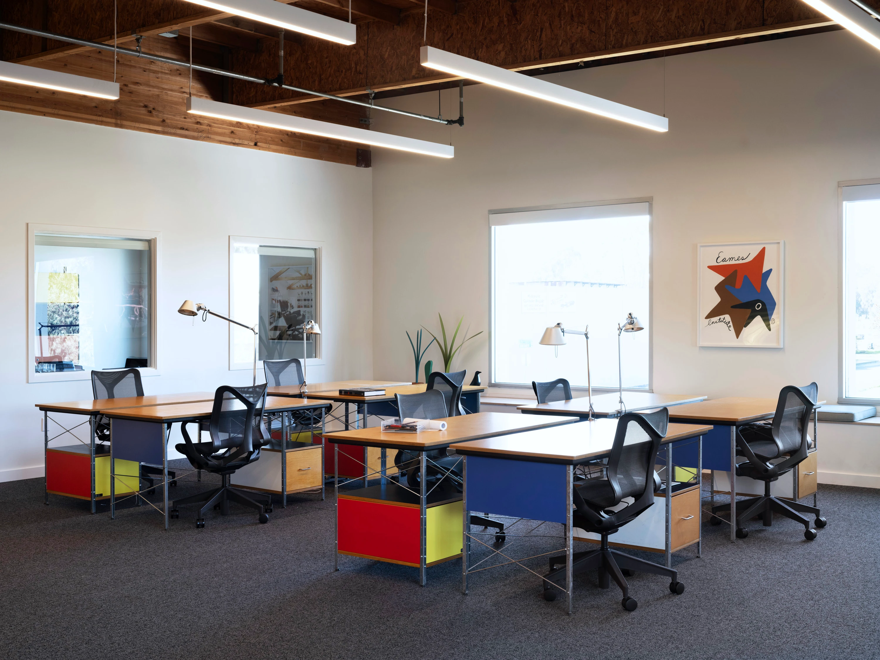 A workspace with several colorful desks at the Eames Institute's Richmond offices.
