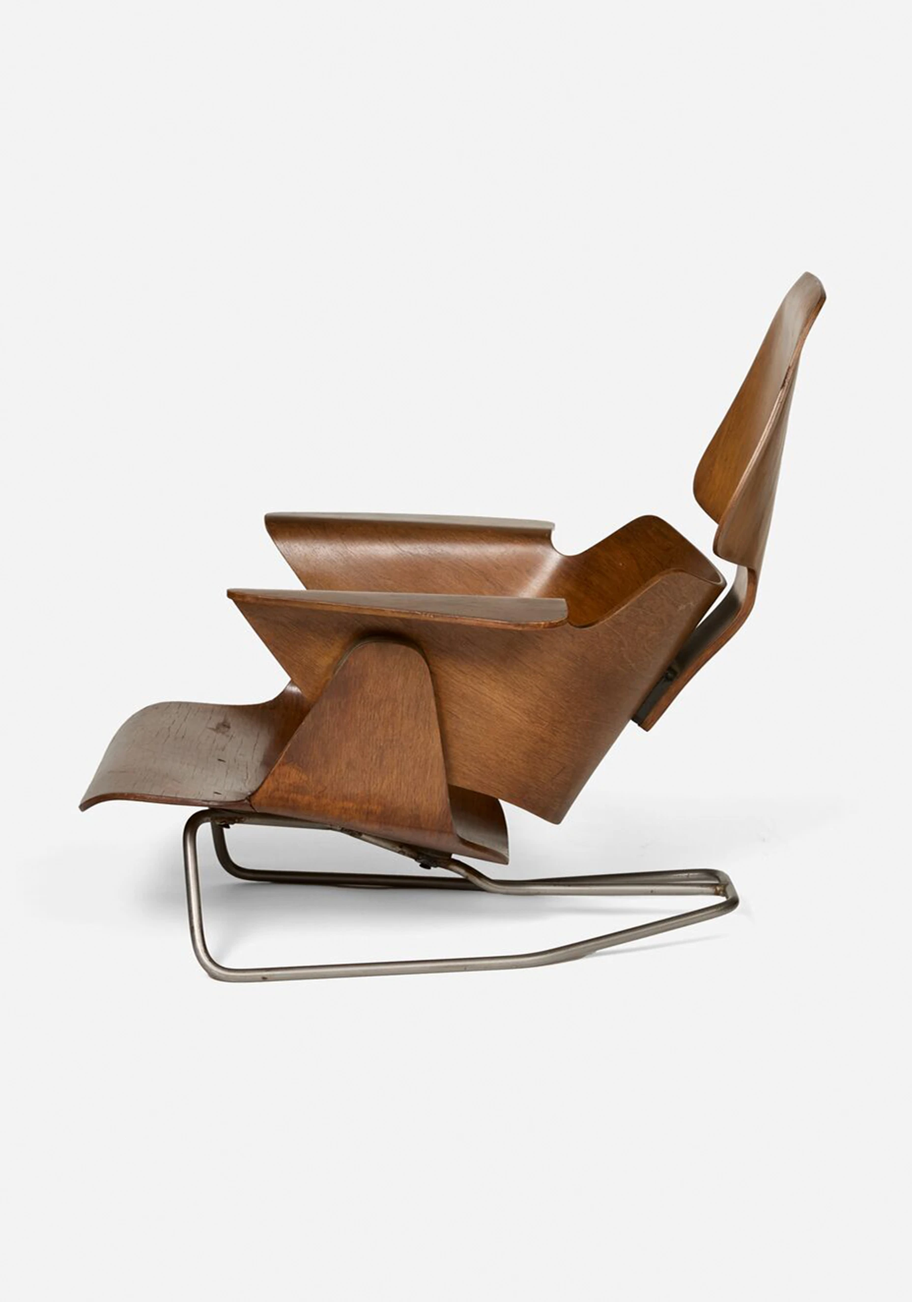 Side view of an Eames Lounge Chair prototype featuring molded plywood and a metal base.