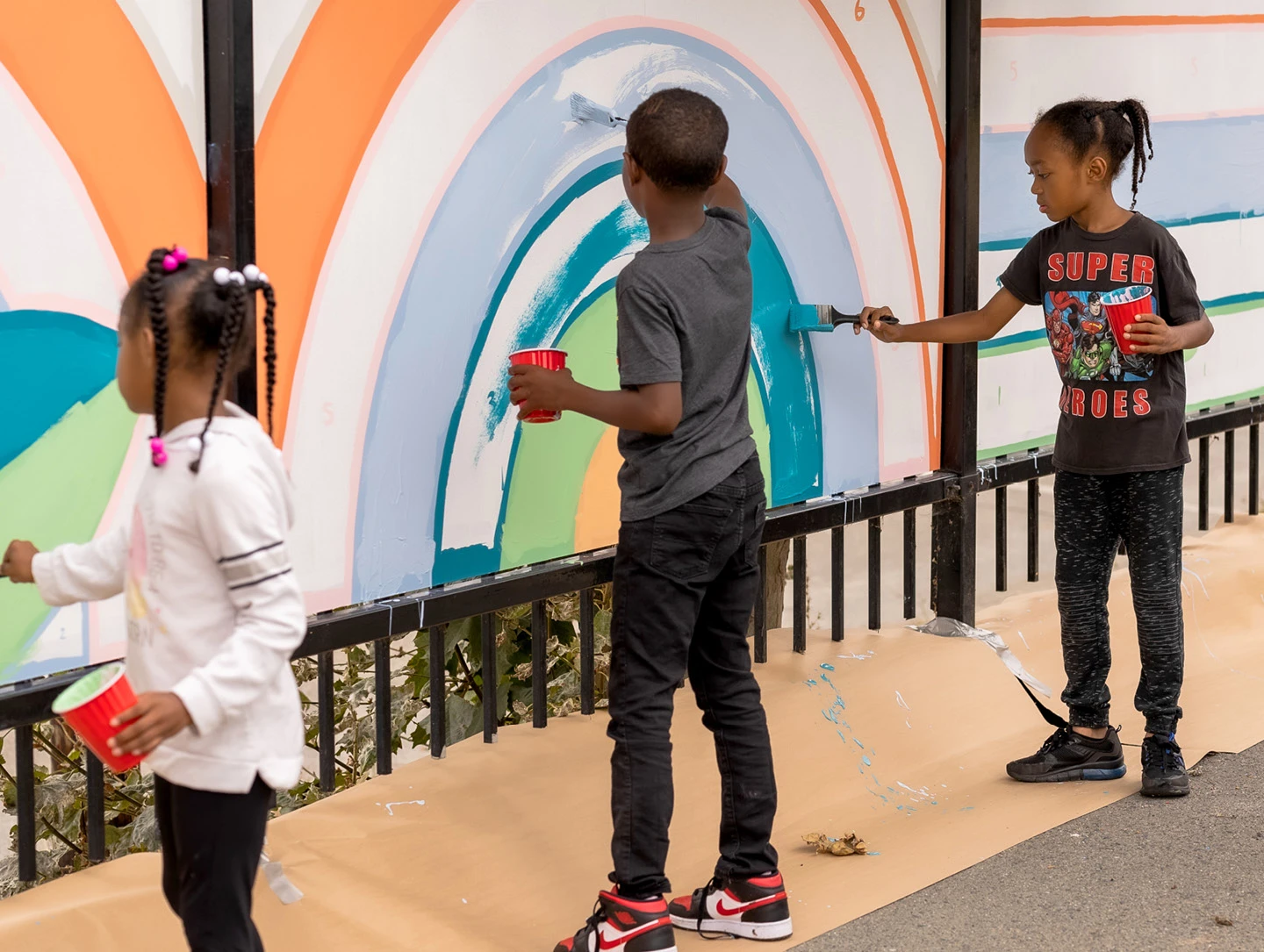 Two students paint brightly colored concentric shapes on a mural wall for Project Color Corps.