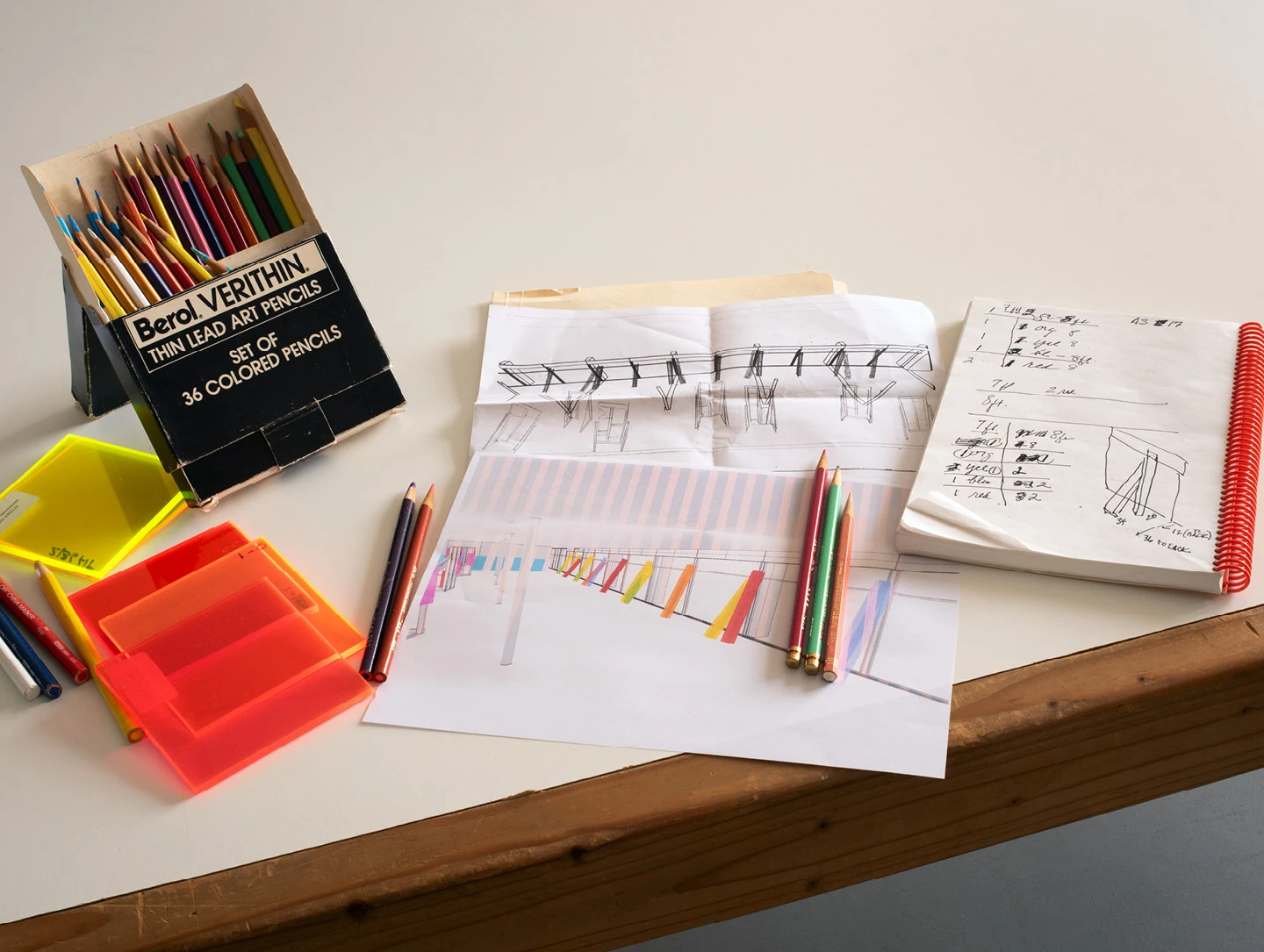 Colored pencils, sketches, and acrylic pieces spread out on a table at artist Barbara Kasten’s studio.