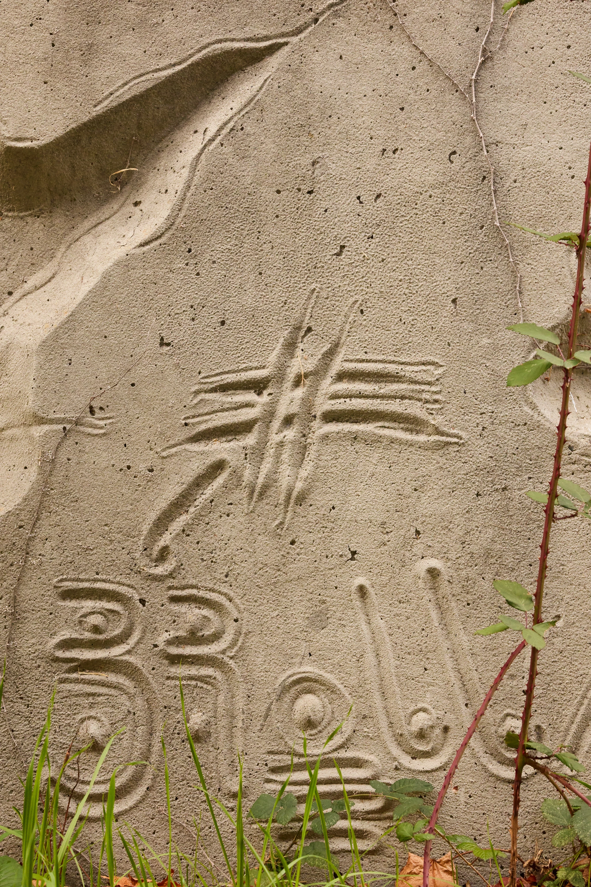 Close up from a carved concrete relief mural by artist Gurdon Woods featuring concentric and curved symbolic marks.