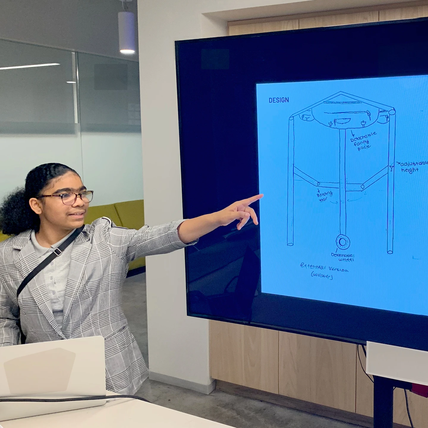 An Inneract Project student who created a walker-cane hybrid design pointing to the schematic drawing of her design.