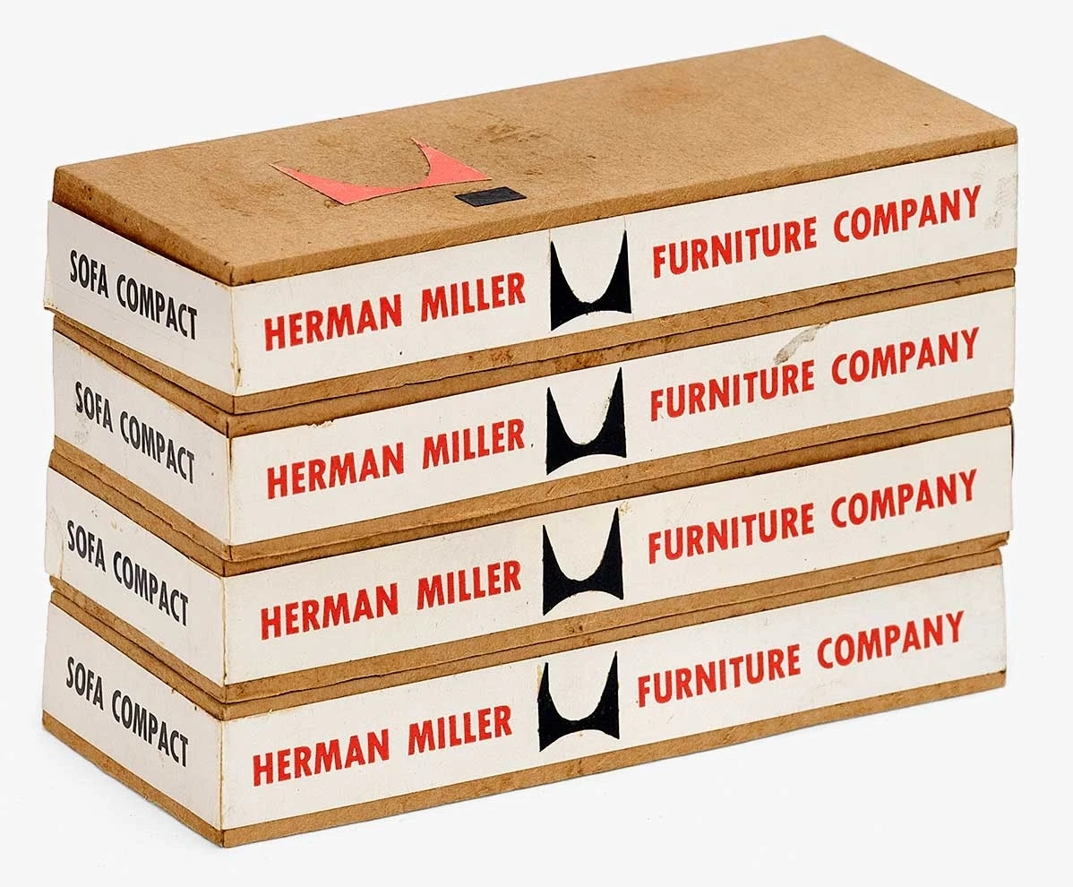 Four Eames Sofa Compact packaging mock-ups in a tall stack with the Herman Miller logo and name prominently displayed.