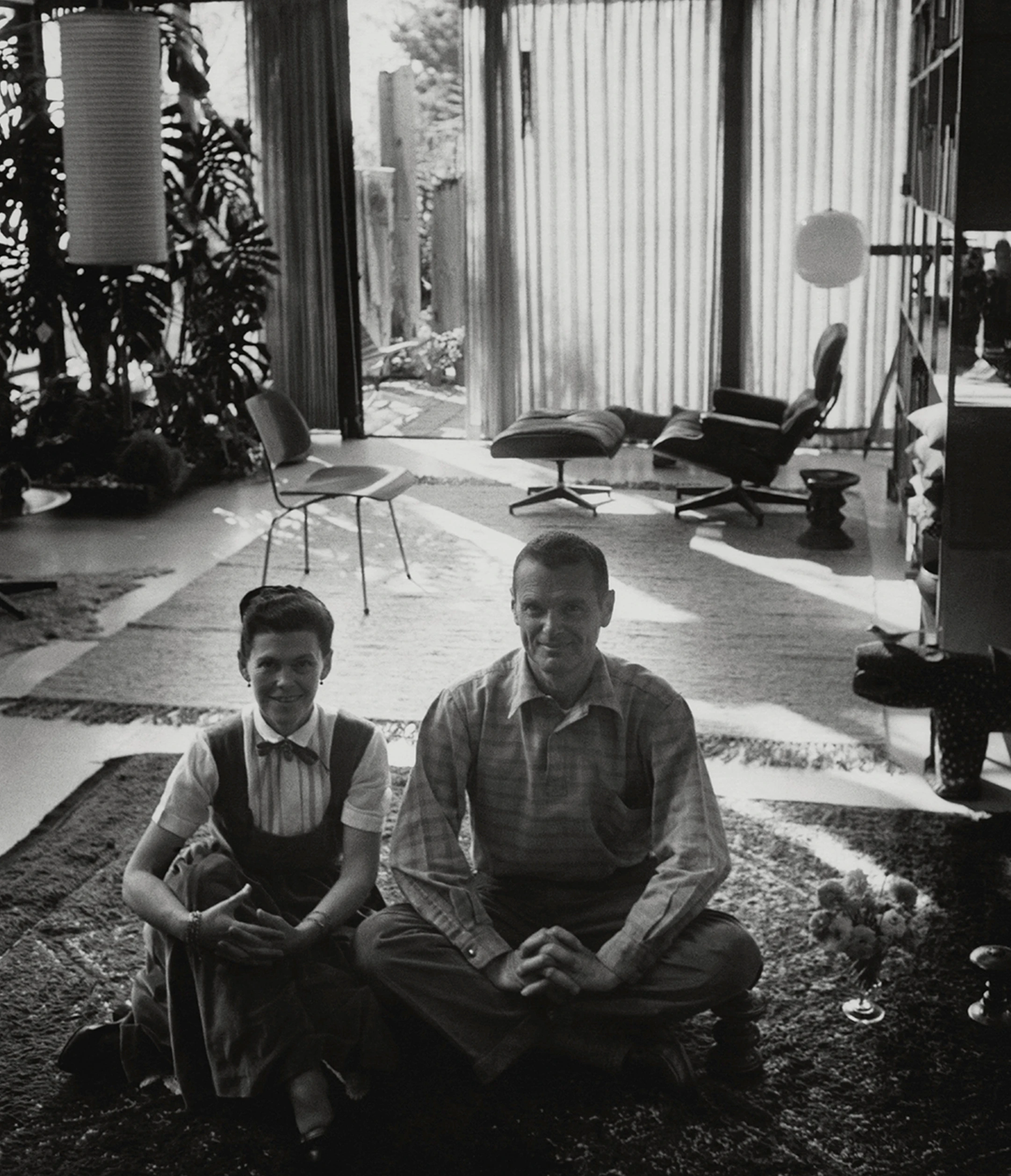 Front view of Ray and Charles Eames in the living room of the Eames House with their furniture designs in the background.