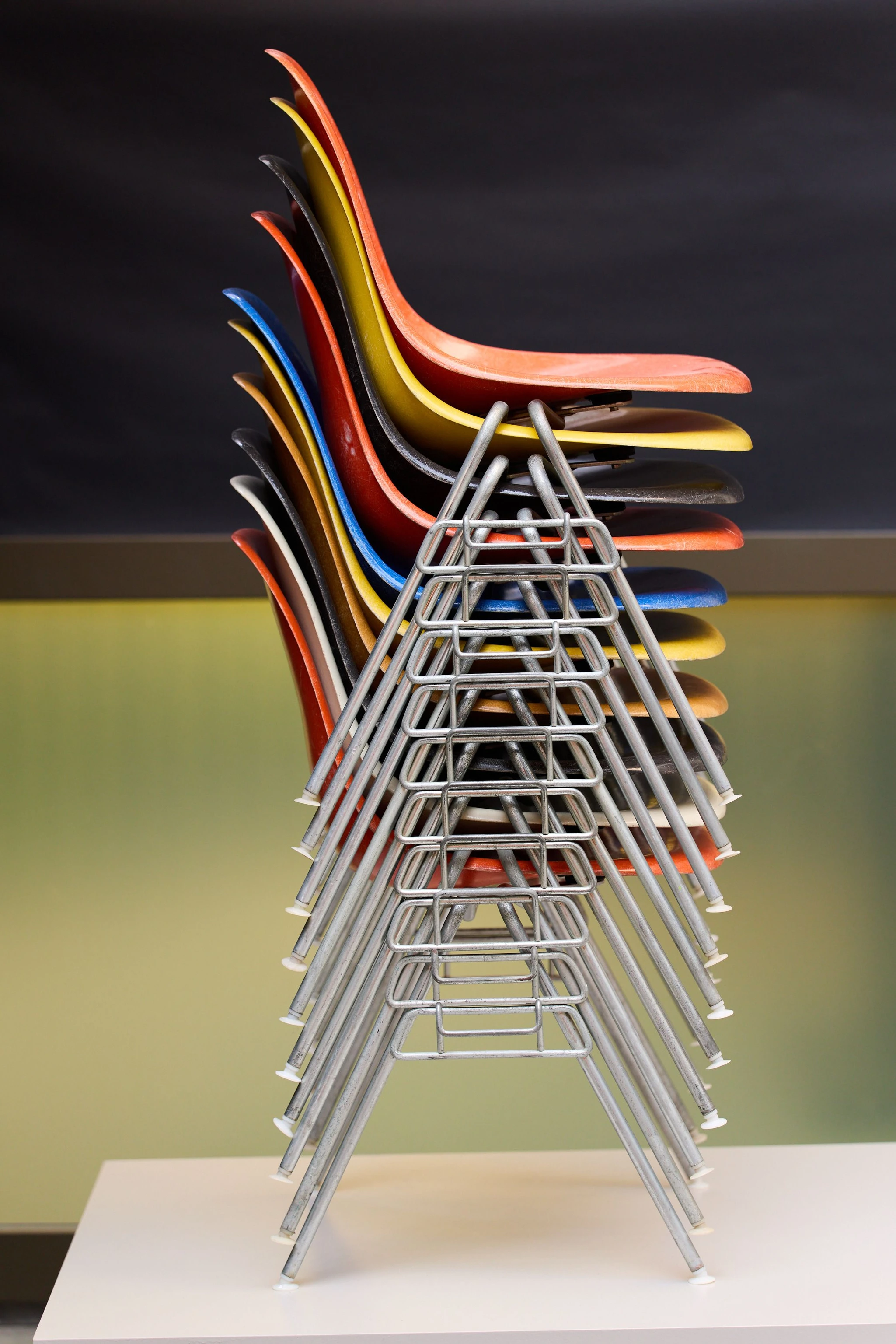 Several colorful Eames DSS chairs stacked on top of each other.