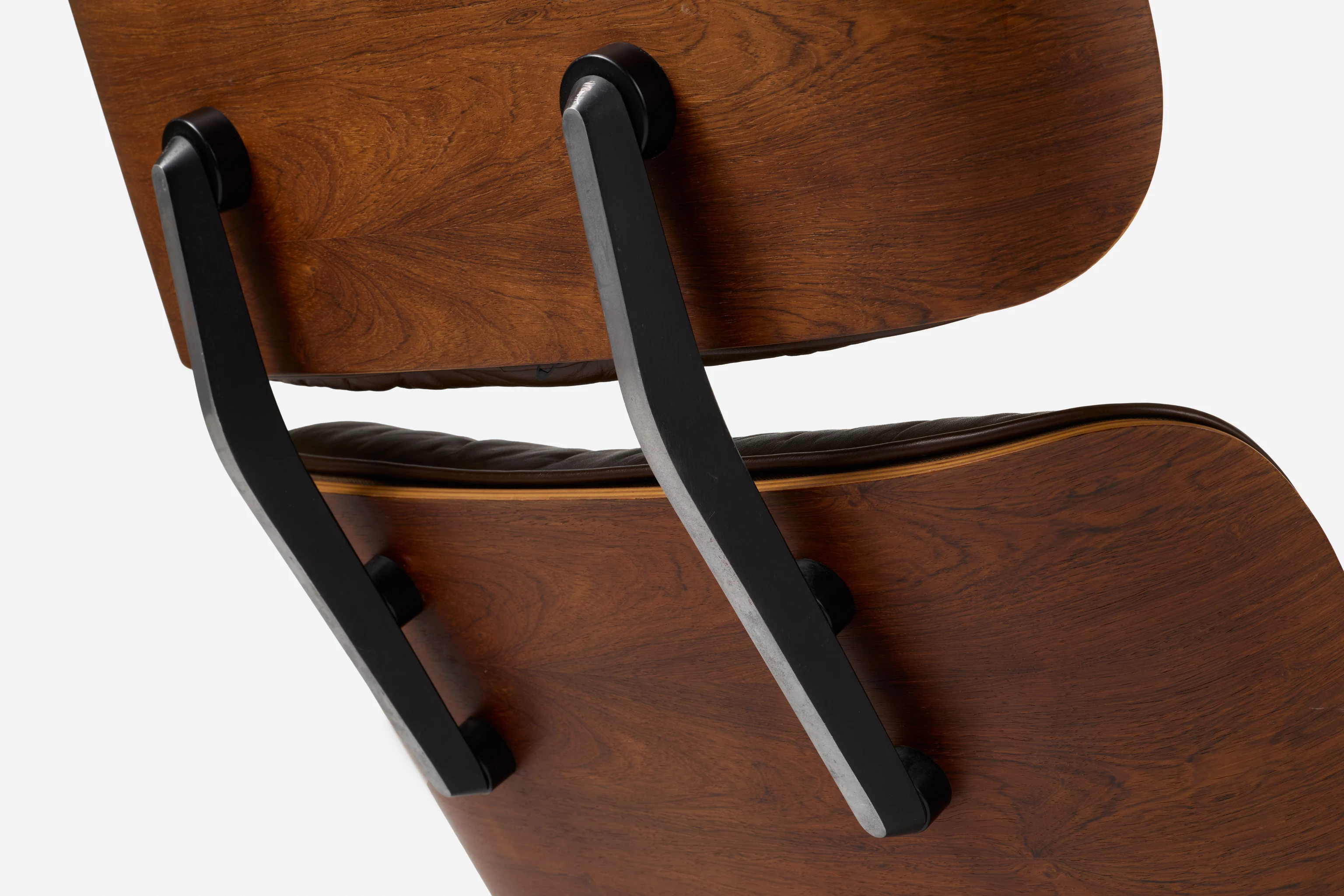 Angled back view of an Eames Lounge Chair featuring the aluminum back supports attached to molded plywood parts.