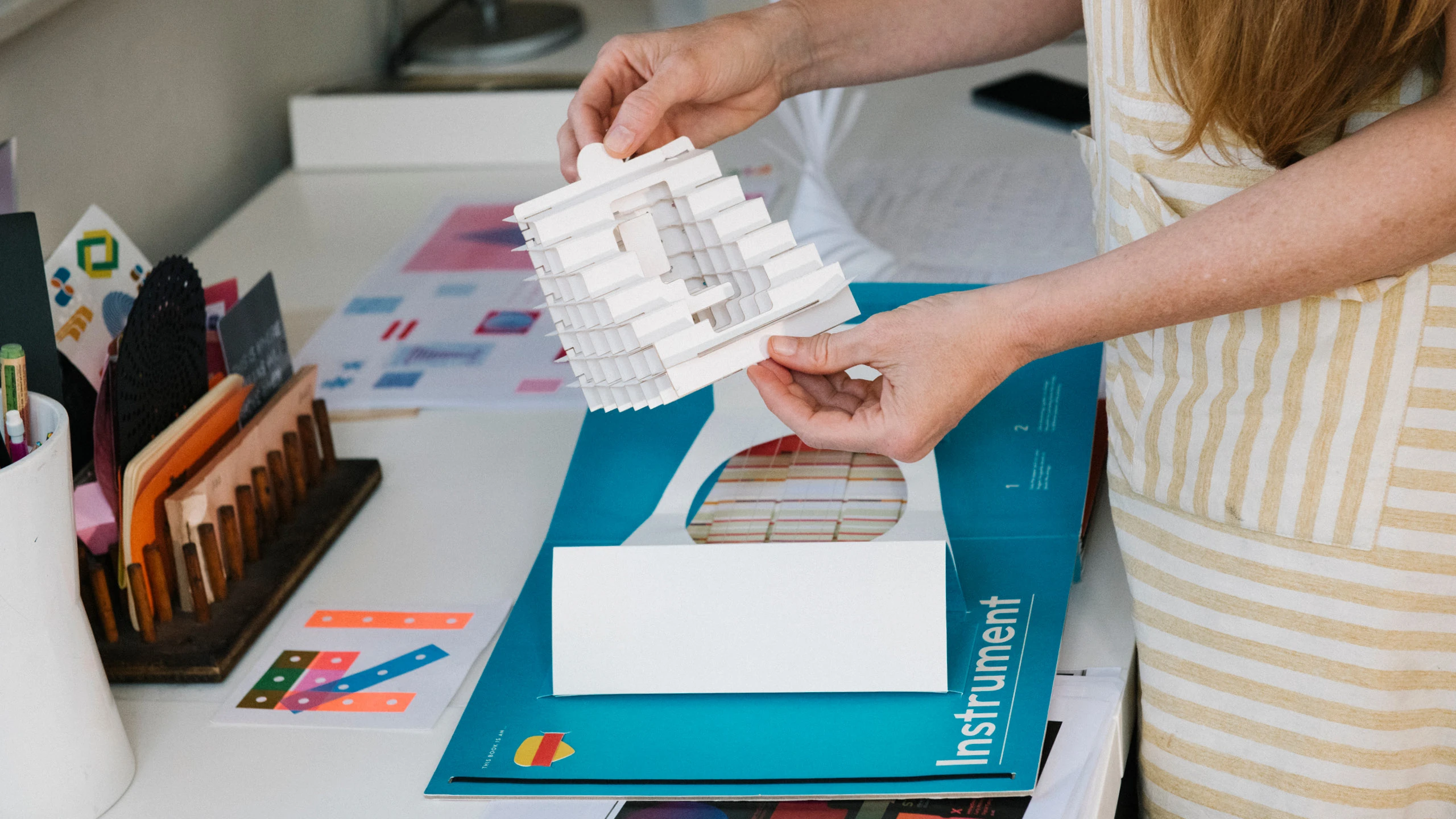 Close up of designer and paper engineer Kelli Anderson’s hands holding a 3-D paper design.