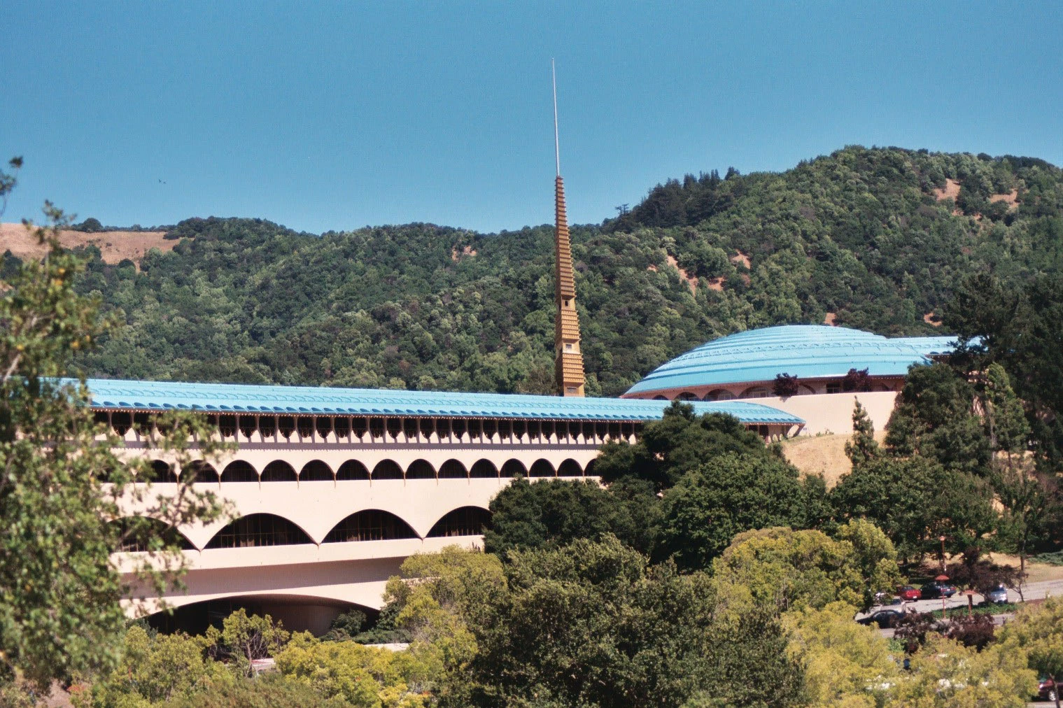 Exterior view of the Marin Civic Center with its blue roof, slender gold spire, and rolling green hills in the background.