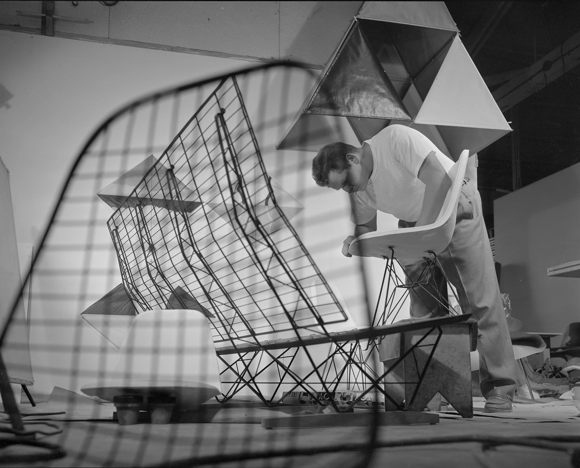 Staff member Don Albinson leans over to work on a fiberglass Eames side shell chair with various Eames chair parts around him.