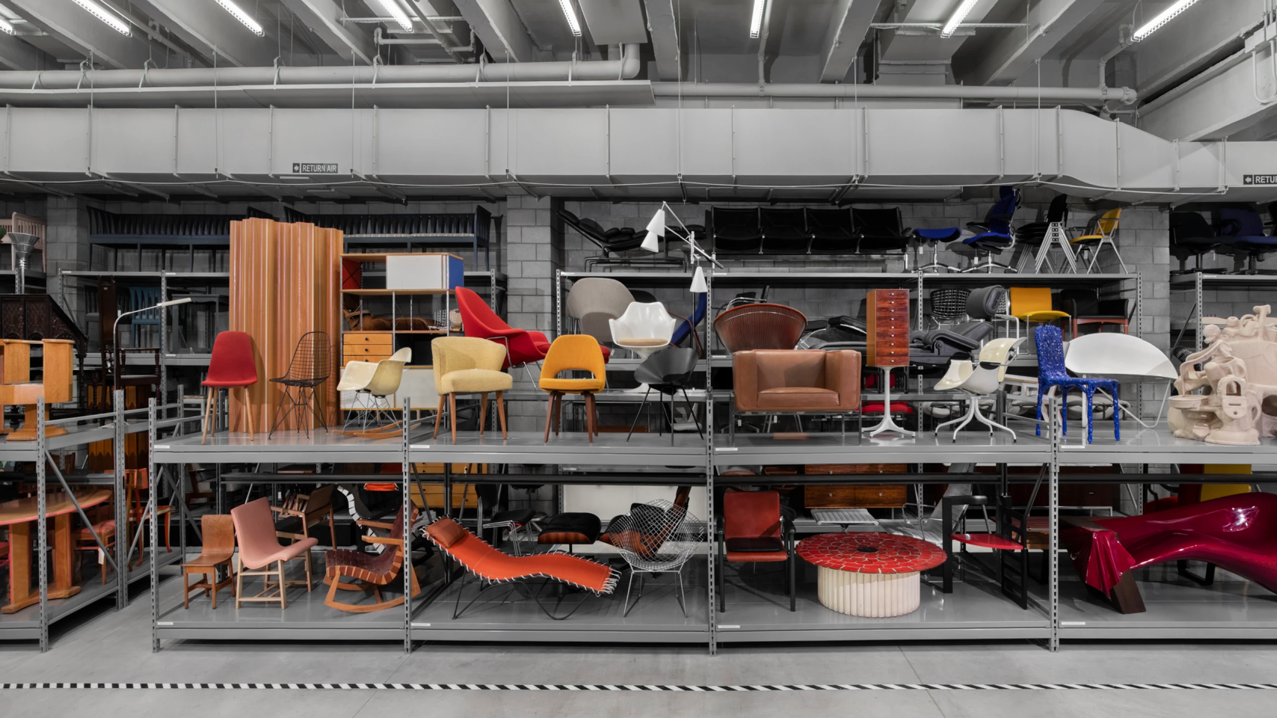 Metal shelves at the Cranbrook Art Museum filled with modern furniture designs, including several Eames chairs.