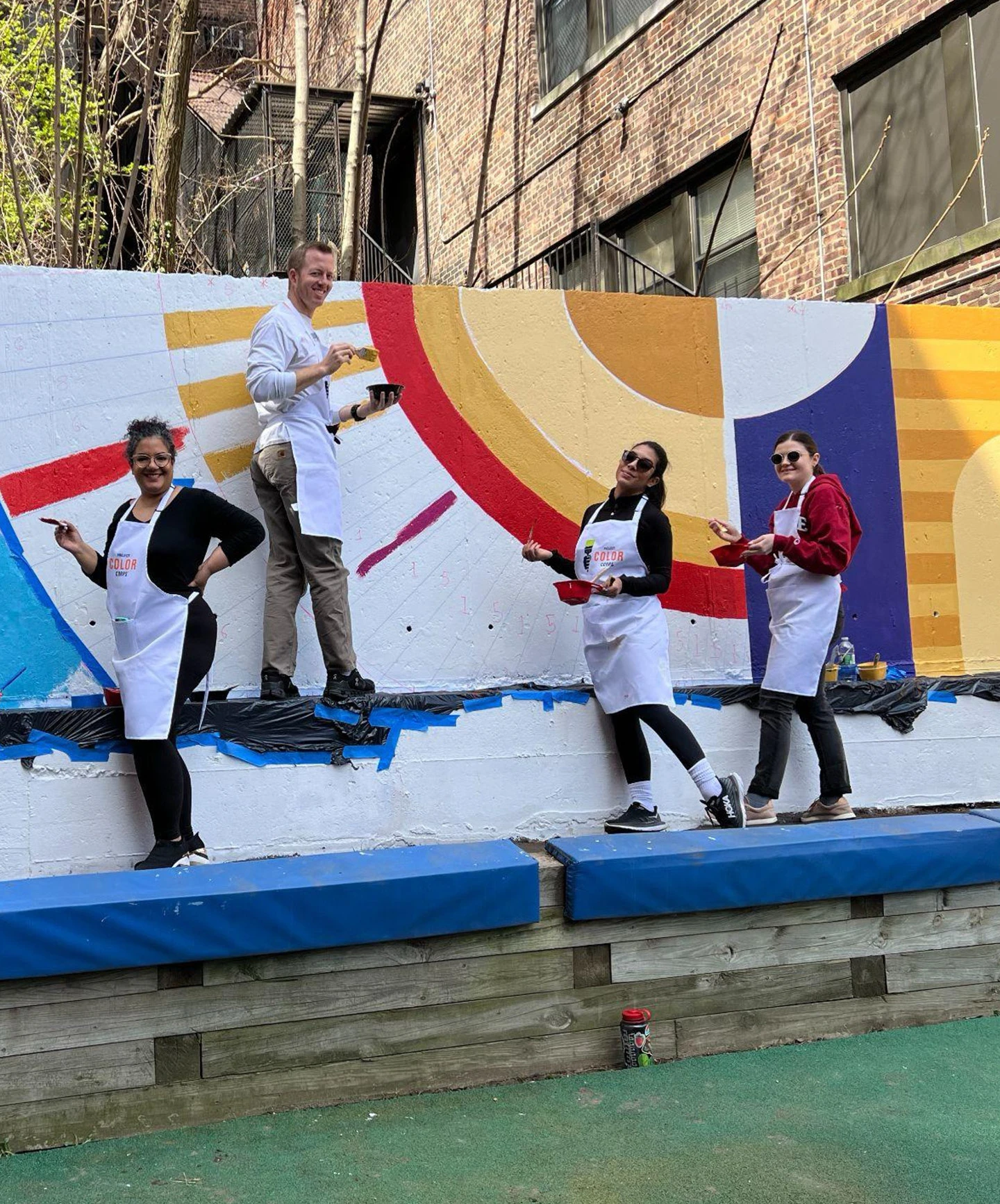 Project Color Corps volunteers standing in front of a colorful mural while they paint.