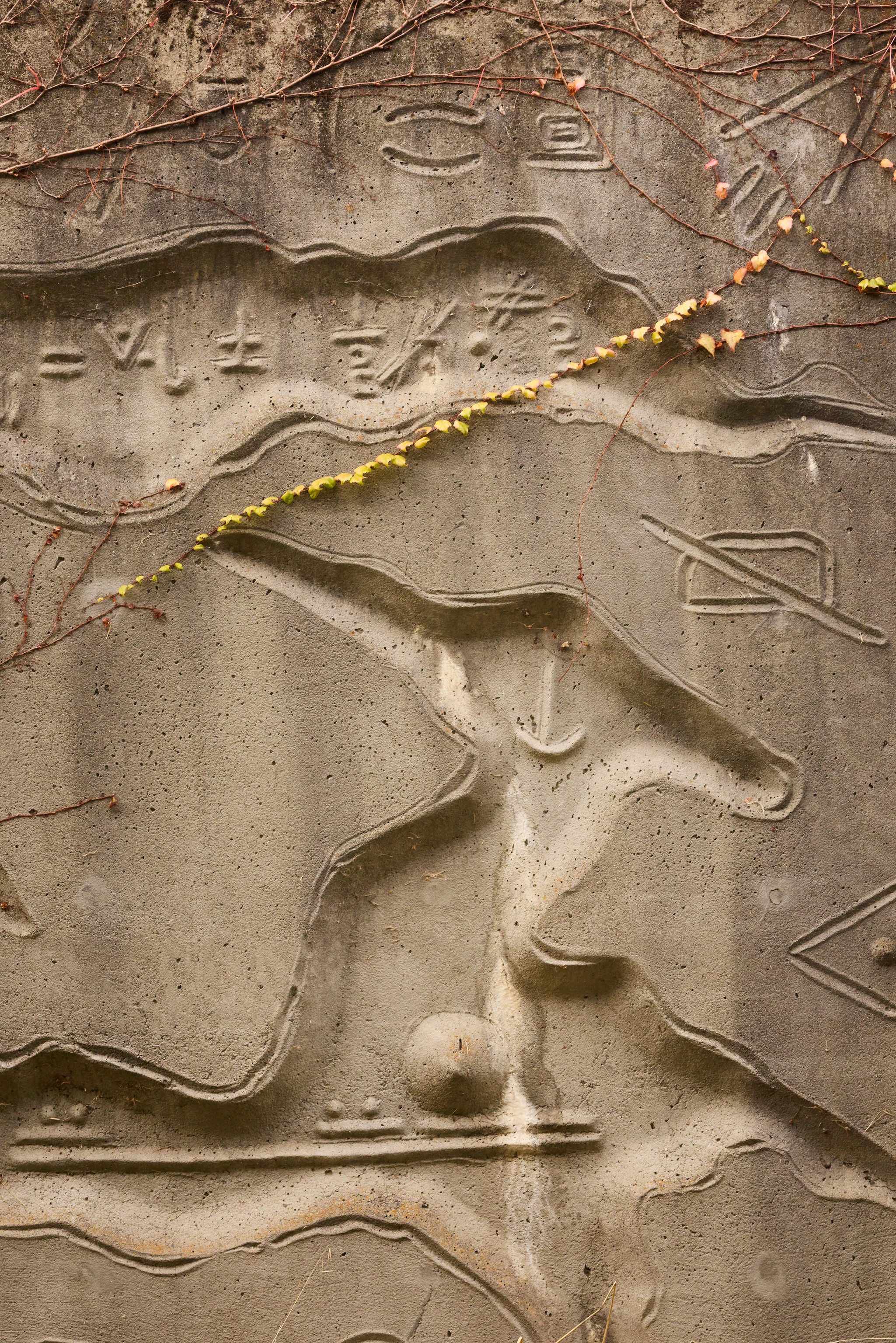 Close up from a carved concrete relief mural by artist Gurdon Woods featuring symbolic marks and bird-like forms.