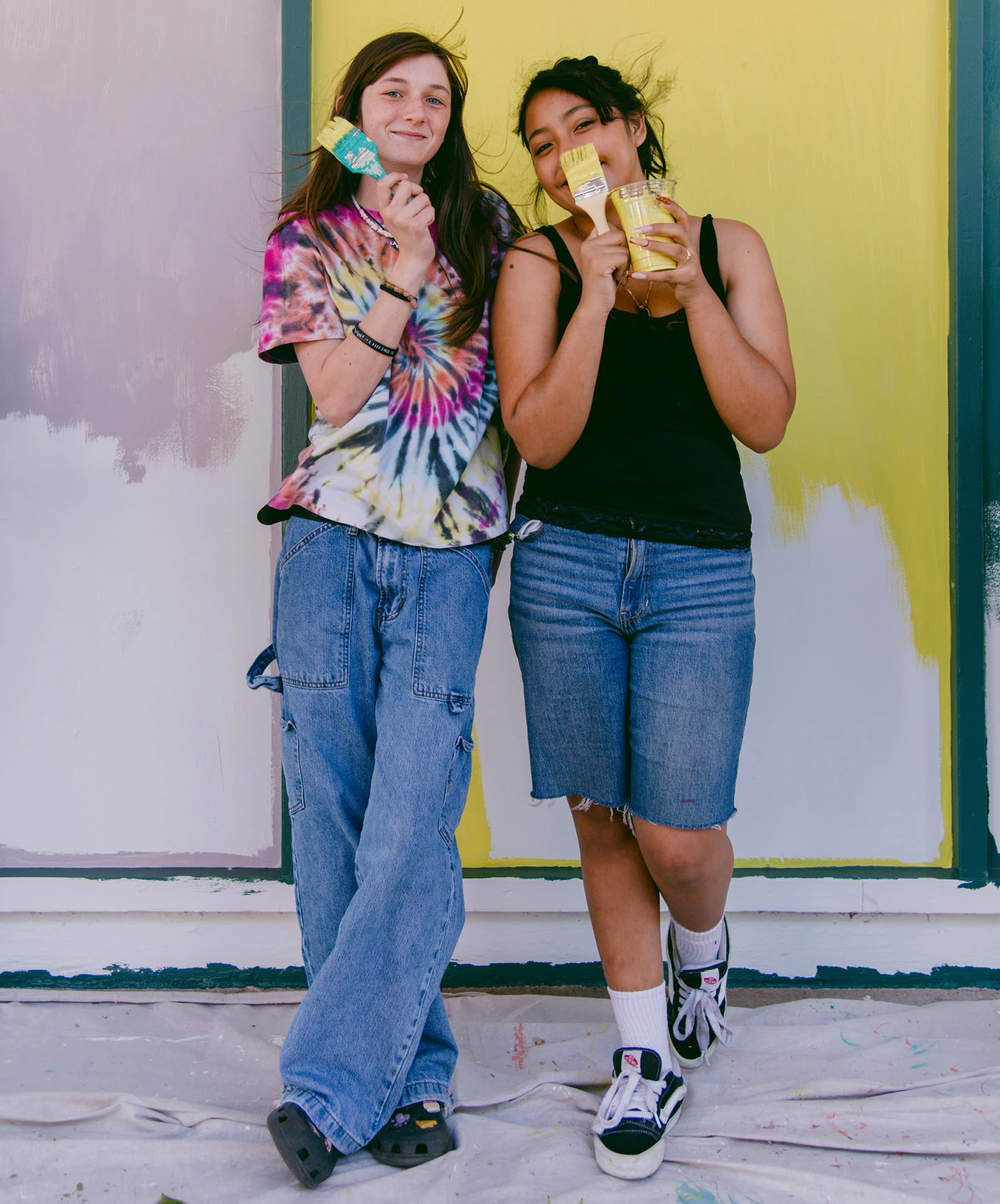 Two student volunteers for Project Color Corps standing in front of a brightly colored mural they painted.