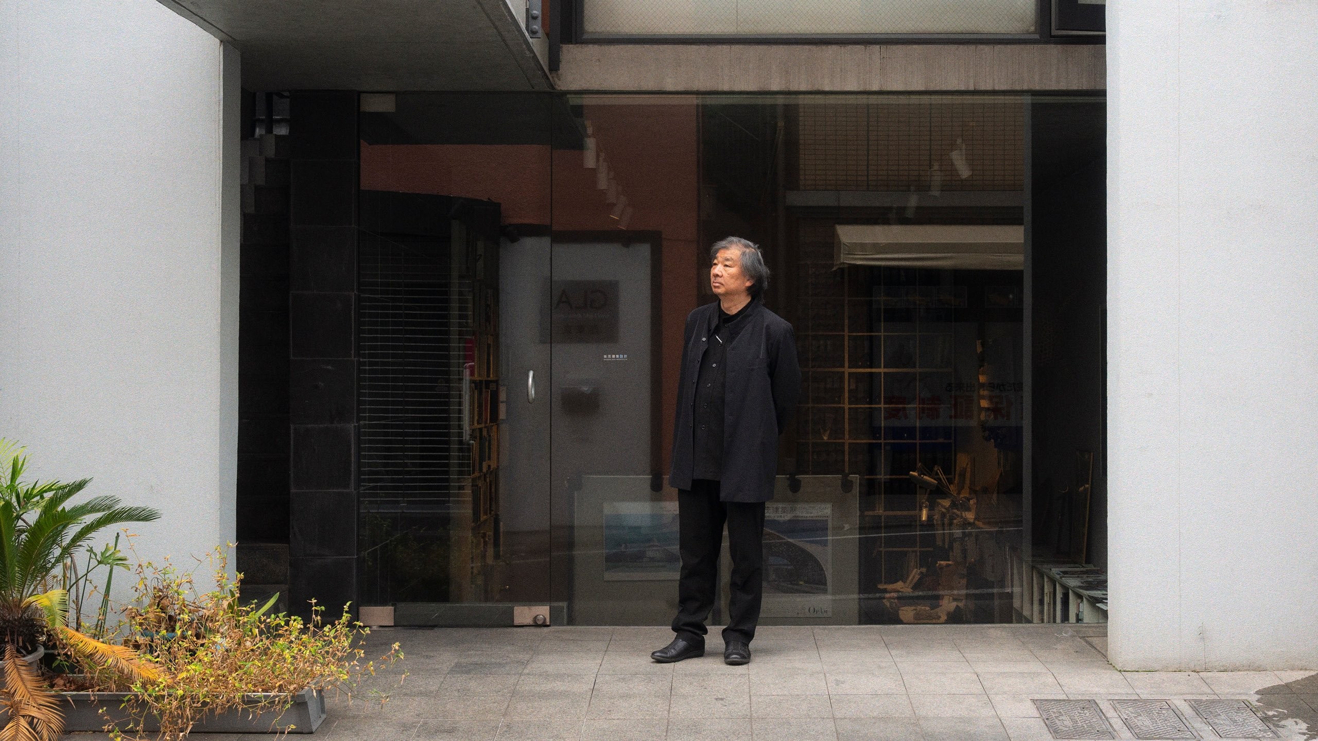 Shigeru Ban standing in front of the glass entrance of the Tokyo office of Shigeru Ban Architects.