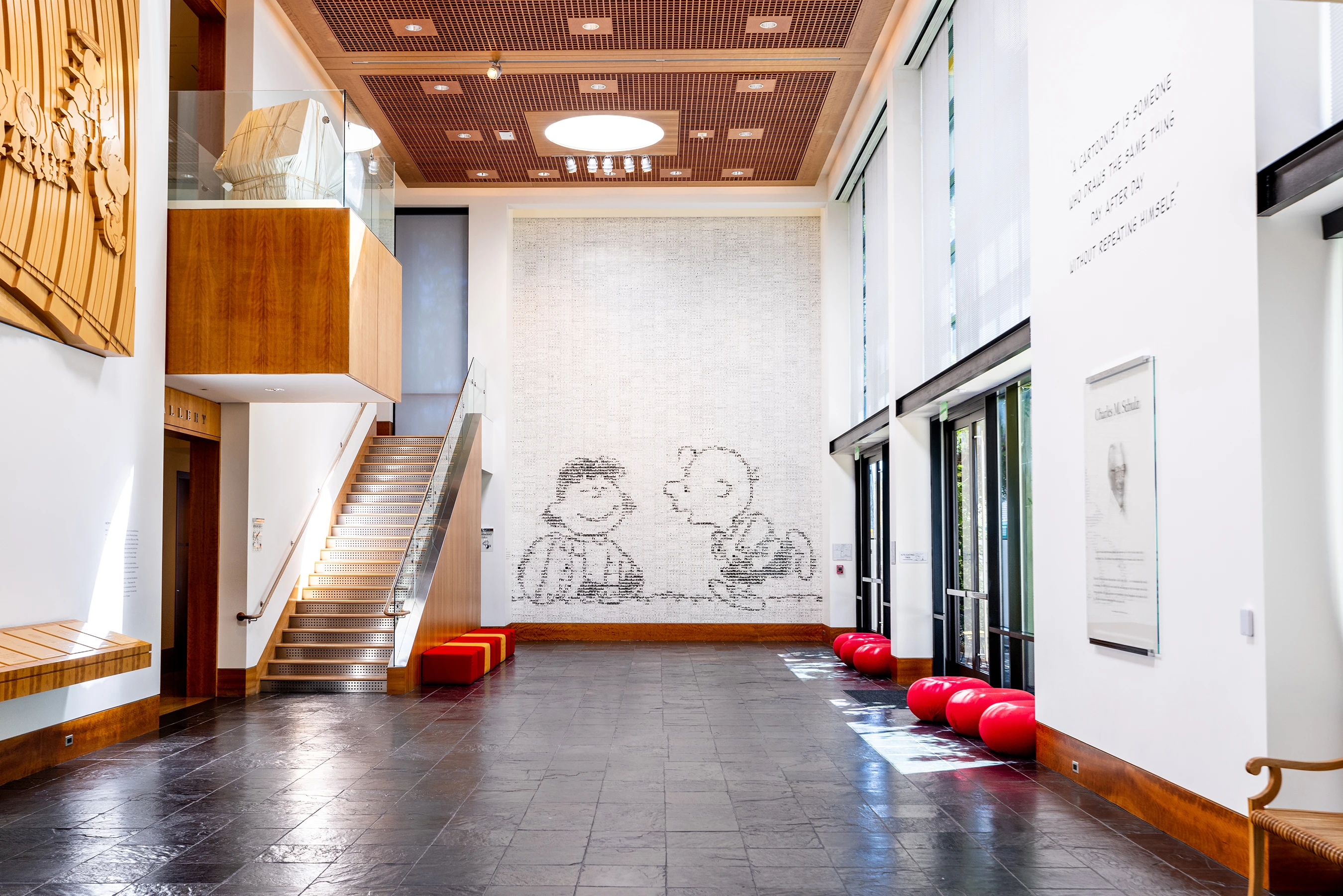 Interior of the Charles M. Schulz Museum featuring a large mural of Charlie Brown and Lucy, red benches, tall windows, and a staircase leading to the upper level.