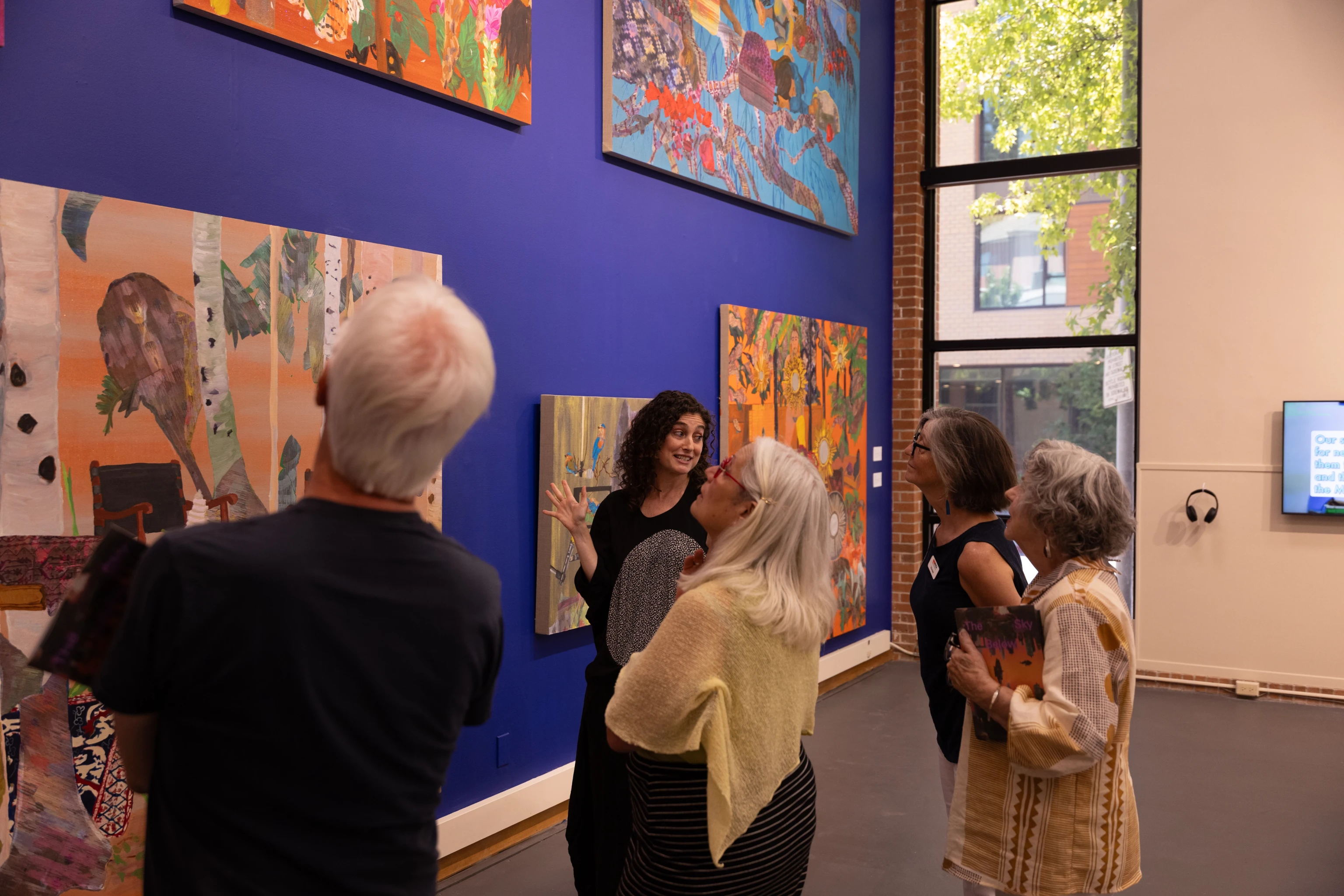 A small group of visitors looking at contemporary paintings displayed on a bright blue gallery wall inside the Museum of Contemporary Art in Marin.