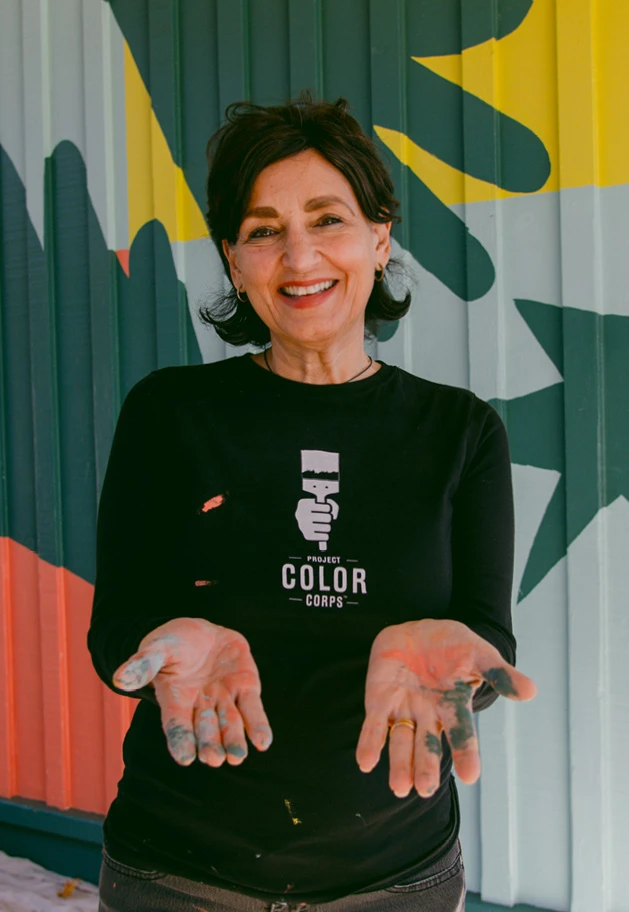 Laura Guido-Clark, founder of Project Color Corps, standing in front of a brightly colored mural.