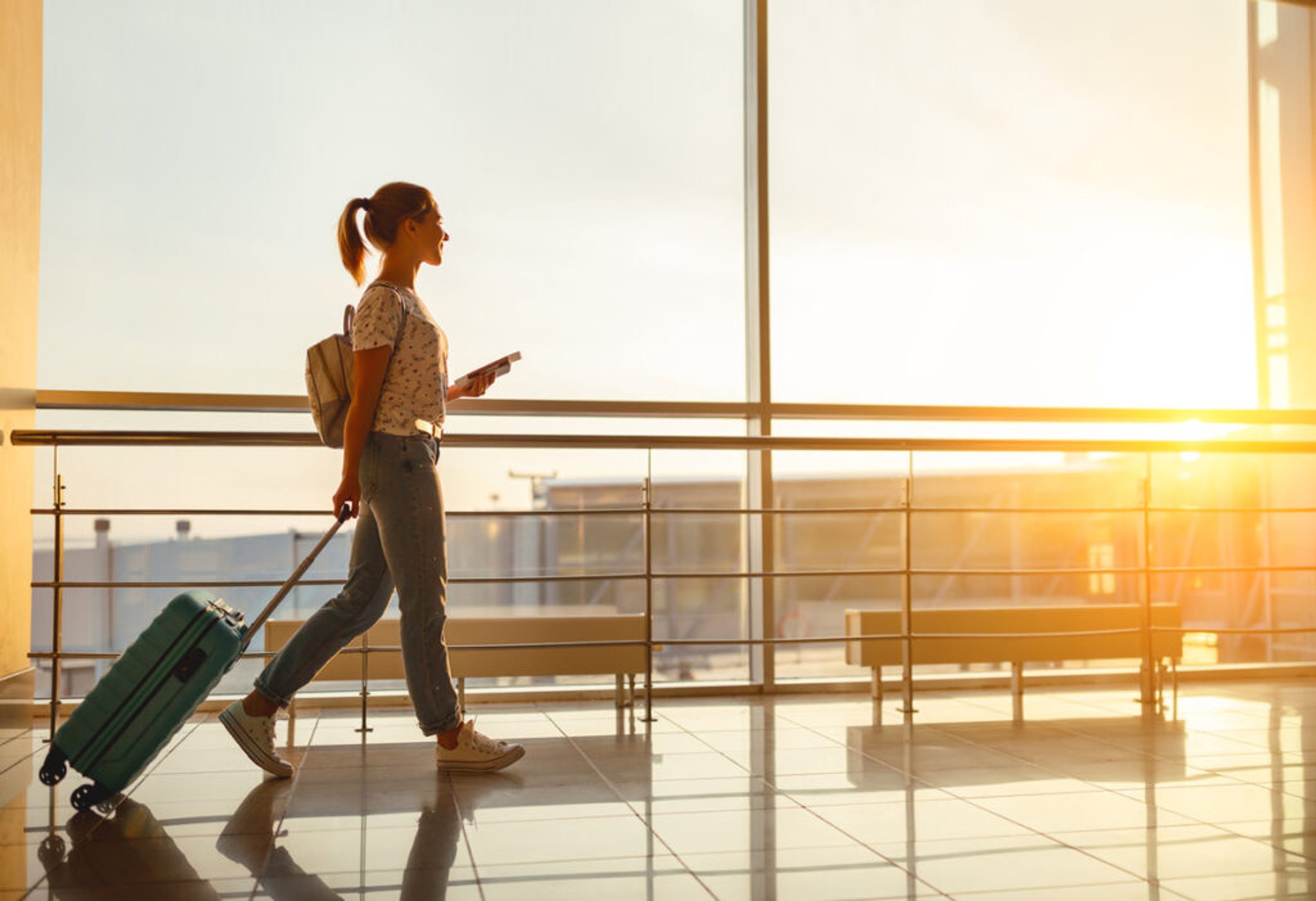 young woman goes at airport at window with a suitcase waiting for plane