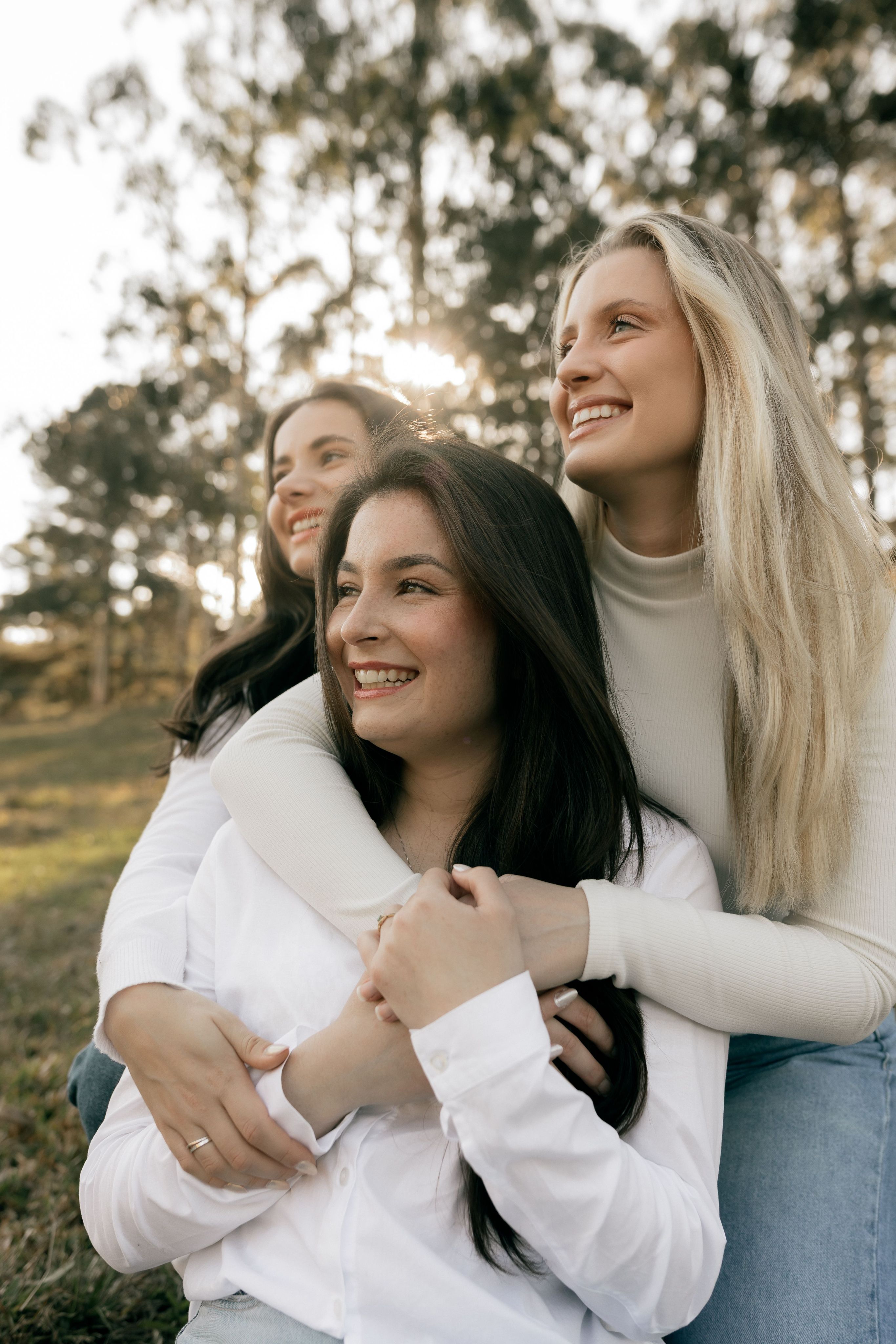 Three women embracing outdoors in bright light