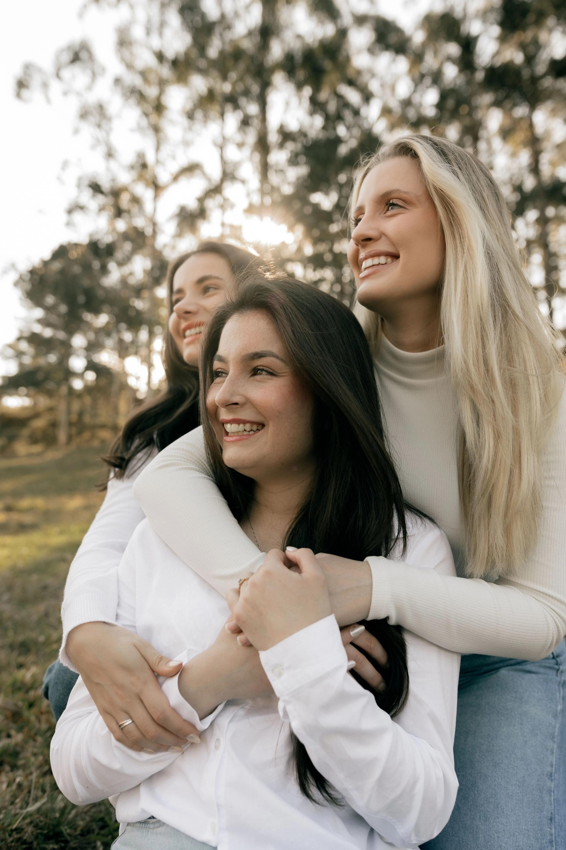Three women embracing outdoors in bright light